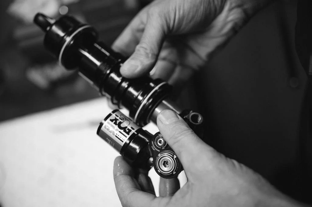 Close-up of hands working on a mountain bike shock absorber, with a focus on the components.