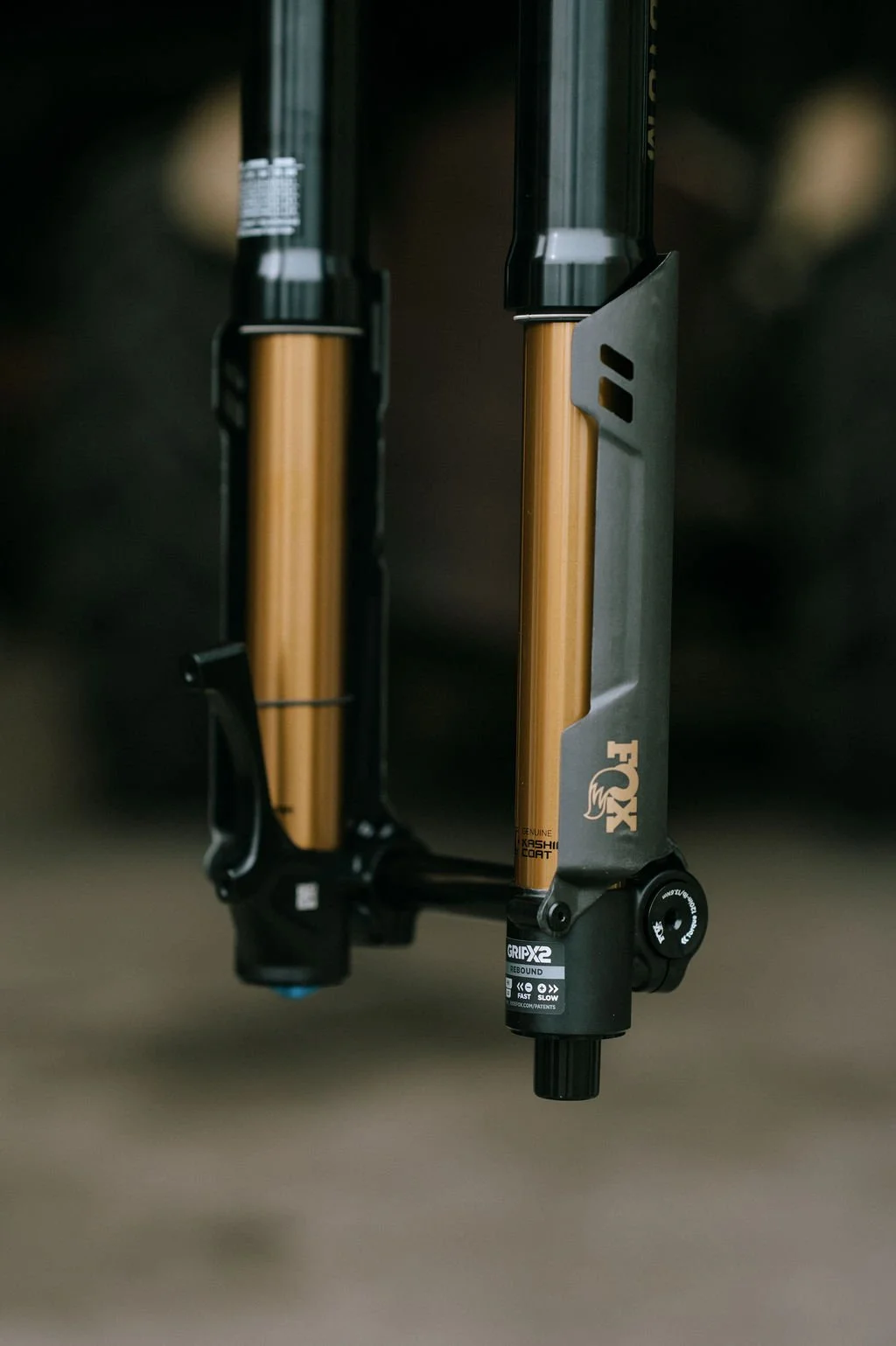 Close-up of suspension fork on a mountain bike, featuring gold-colored stanchions and black lower legs with FOX branding.