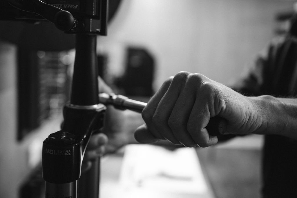 A close-up of a person's hand tightening a screw on a camera tripod in a workshop or studio.