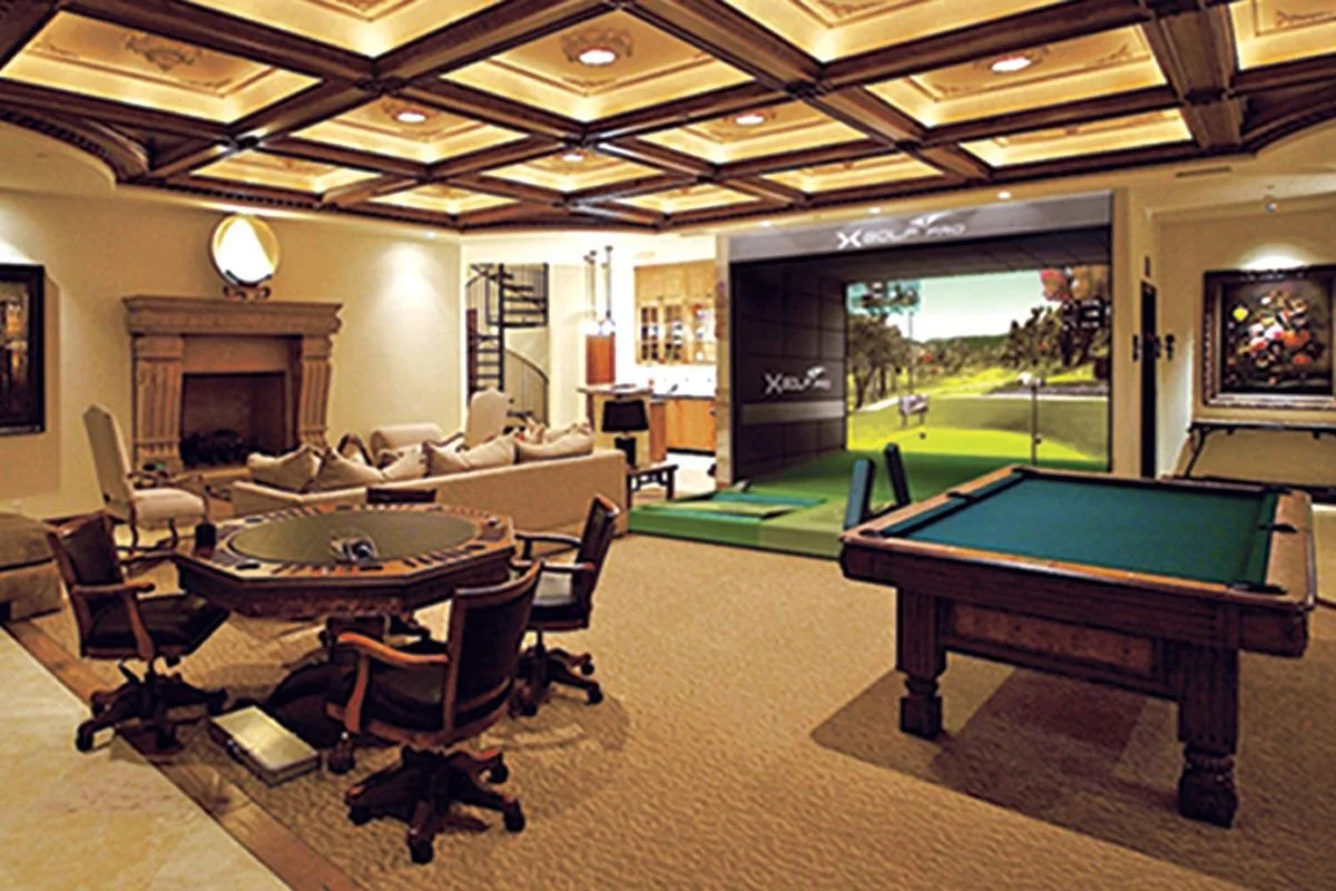 Luxury game room with a poker table, pool table, large projector screen displaying a golf video game, couch seating area, and artwork on the walls.