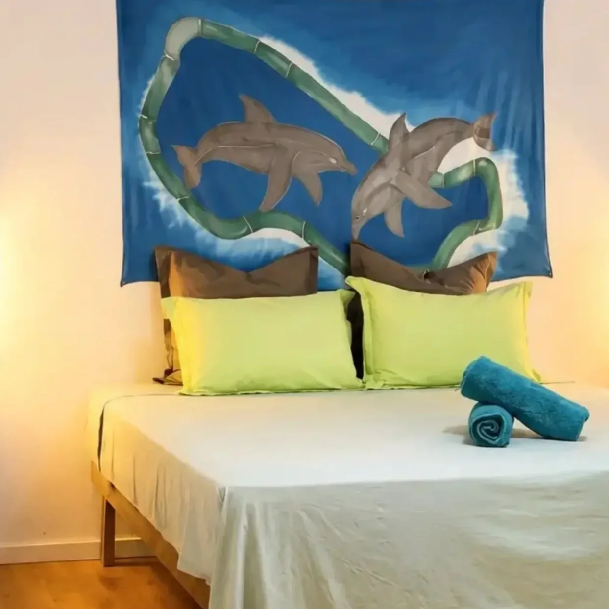 Chambre climatisée avec lit double, deux coussins verts à motifs de feuilles, étagères en bois avec serviettes et couverture, lampes de chevet, rideau blanc sur la fenêtre.
