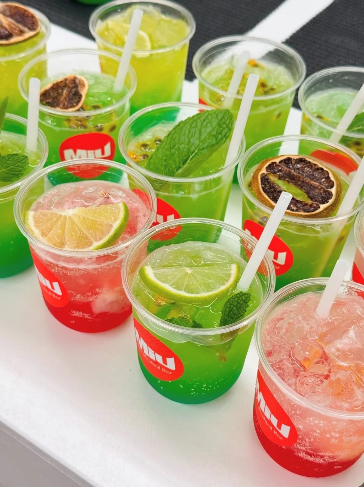 Several cups of colorful fruit-flavored beverages with lime, lemon, mint, and dried citrus slices.