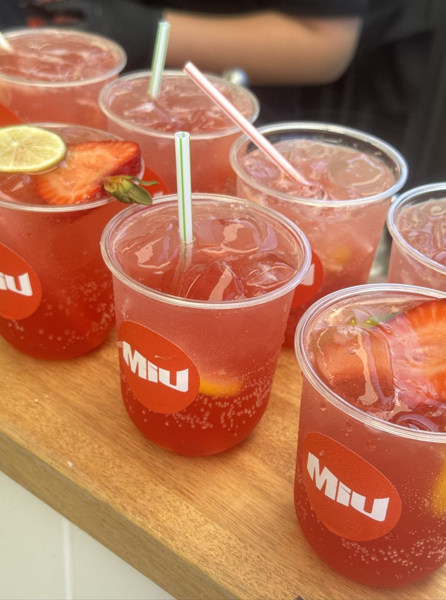 Several cups of pink lemonade with strawberries and lemon slices, some with ice, on a wooden tray.