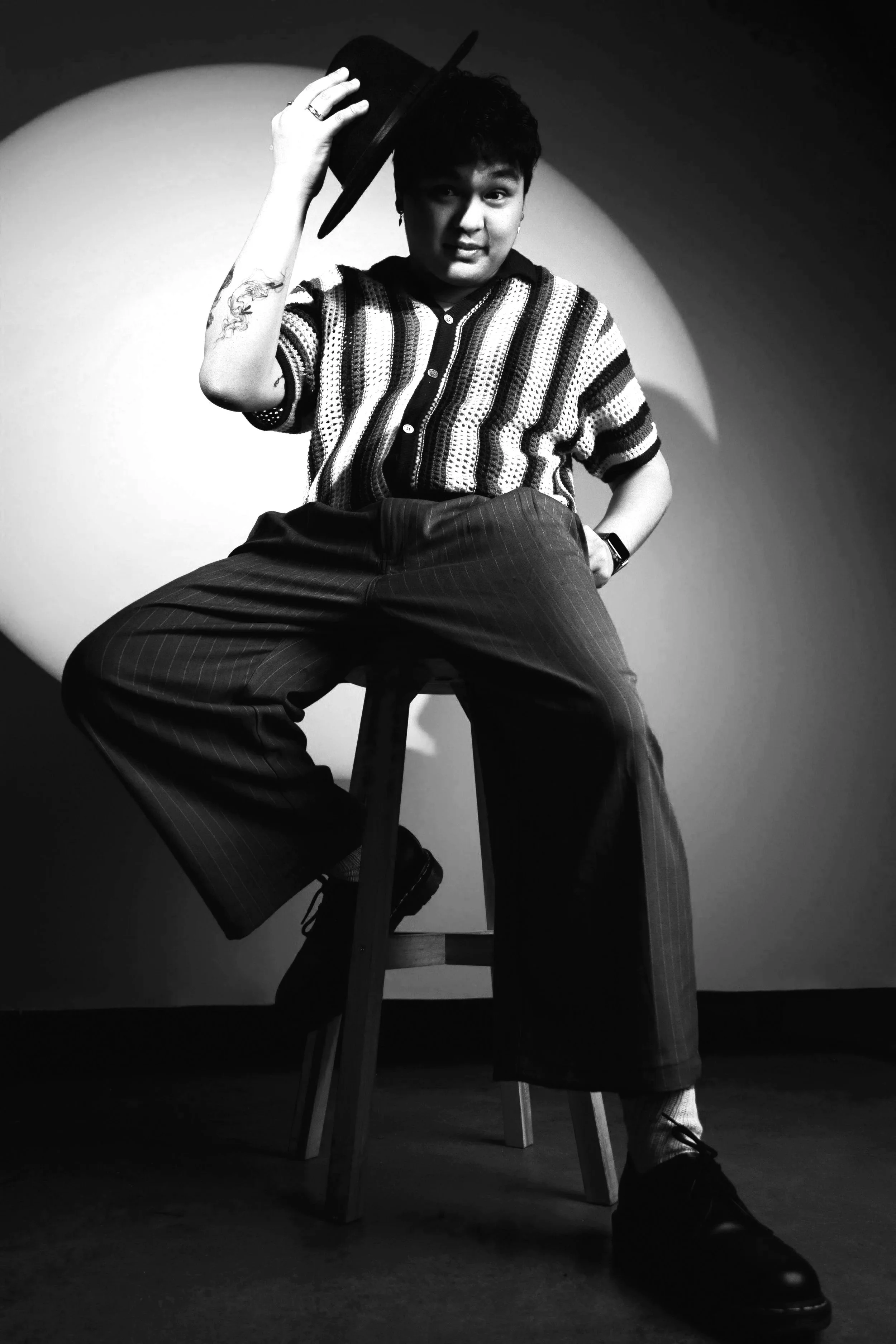 Performance Studios Elite Performance Team member Mark Mirhan wearing a sophisticated outfit with a hat, sitting on a bar stool and posing.