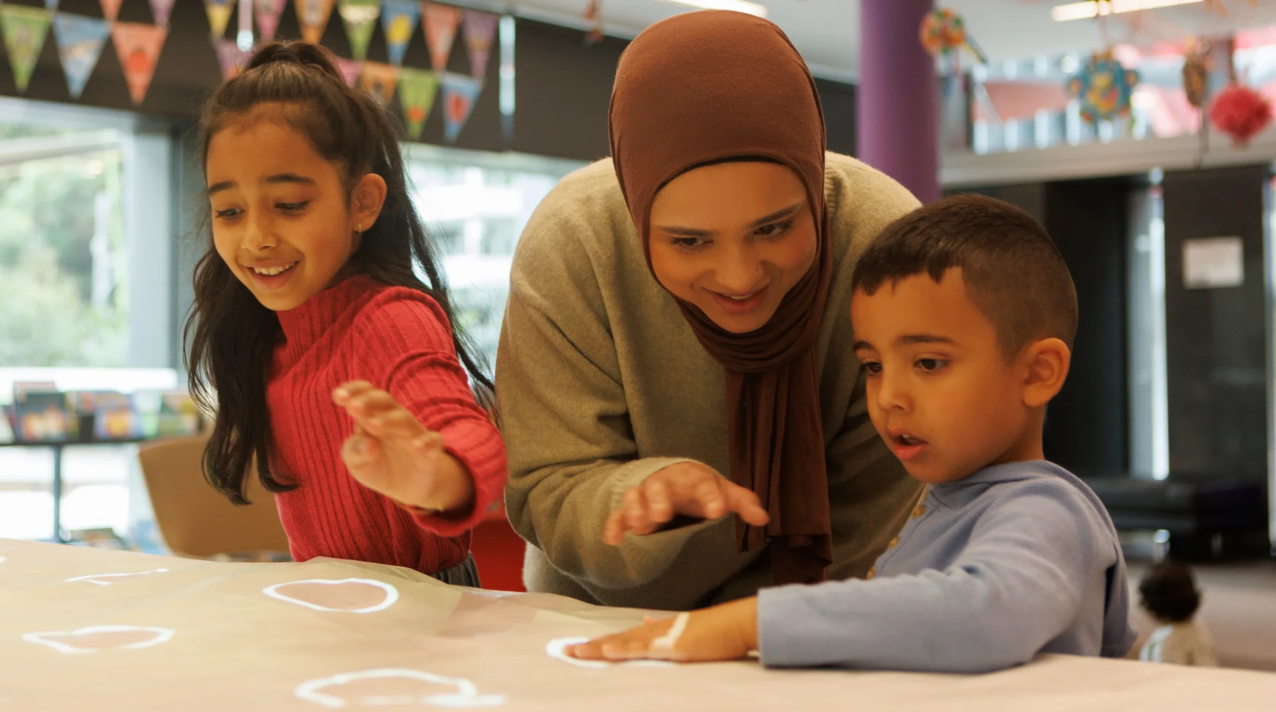 A CALD mother and her two children interacting with a display at their local library