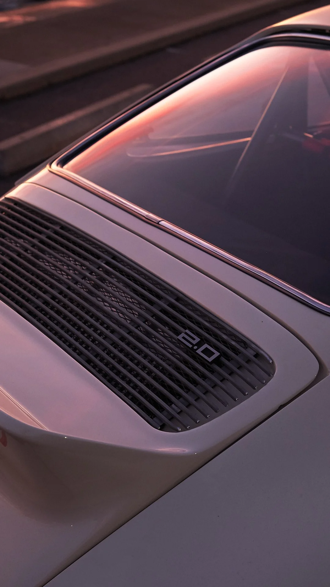 Close-up of the rear section of an old silver Porsche 911 with a sun-warmed windshield reflecting a sunset sky.