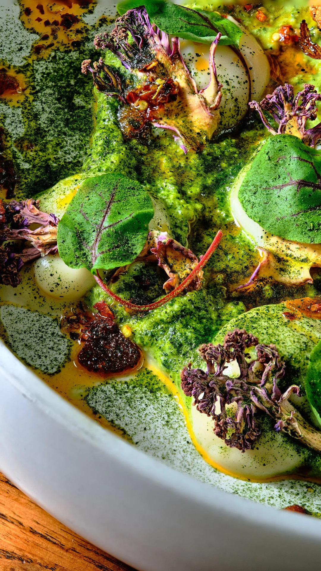 Close-up of a dish with green leafy vegetables, possibly herbs and microgreens, in a creamy sauce garnished with herbs and vegetables.