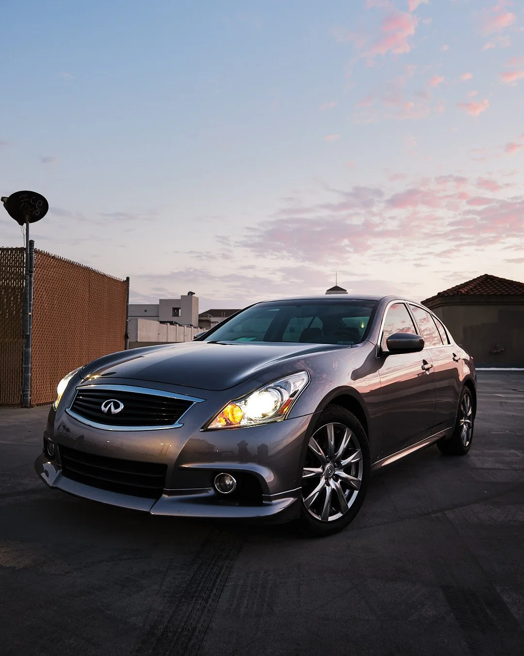 Gray Infiniti sedan parked outdoors during sunset with a partly cloudy sky in the background.
