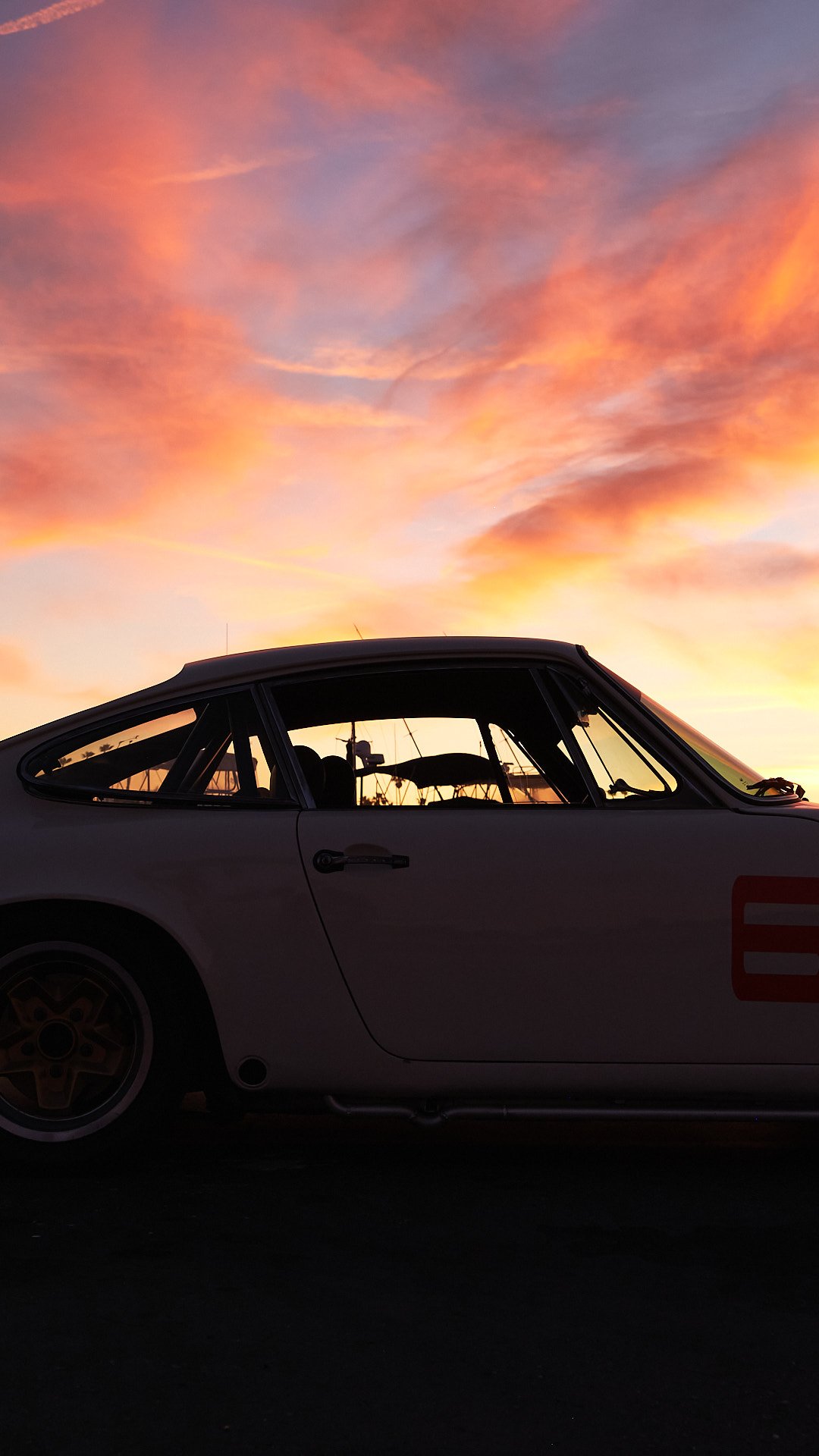 Silhouette of a vintage white race car parked against a colorful sunset sky with shades of pink, orange, and purple.