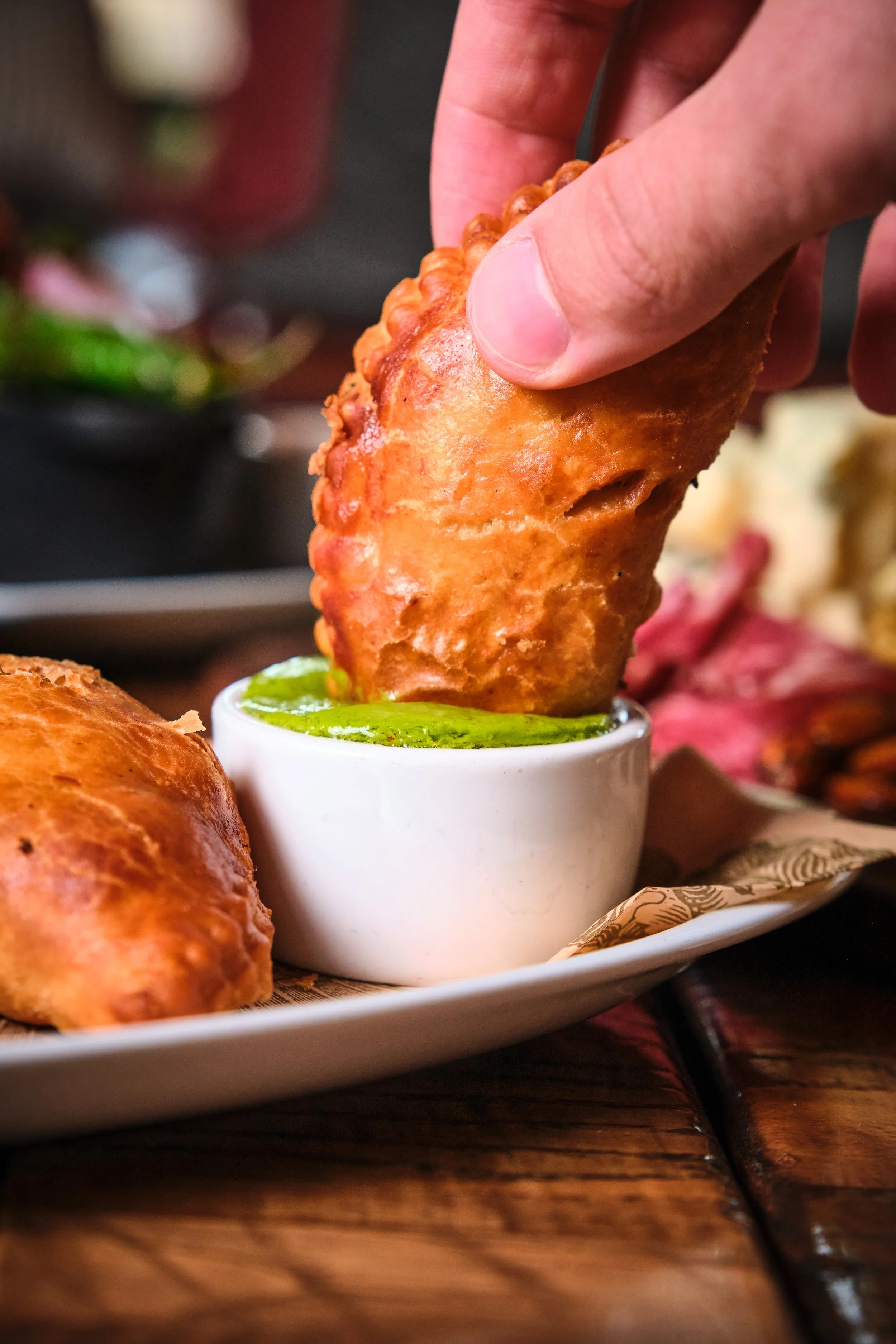 Person dipping an empanada into a small white bowl of green sauce.