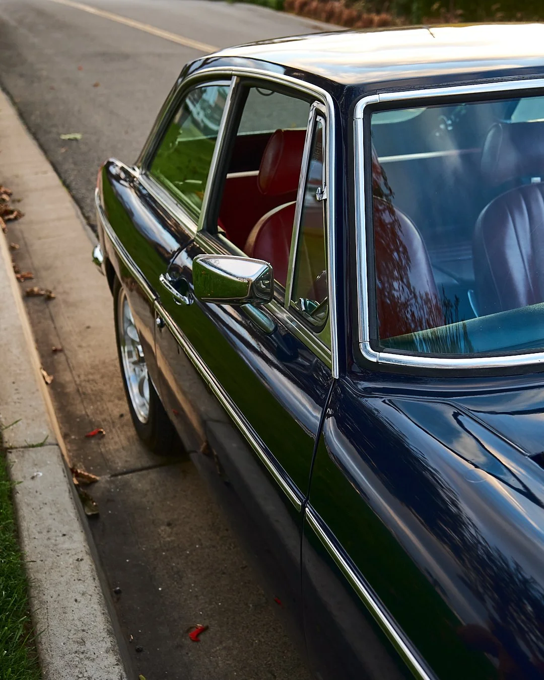 A classic black car with chrome accents parked on the side of a suburban street, reflecting the sky and trees in its shiny surface.