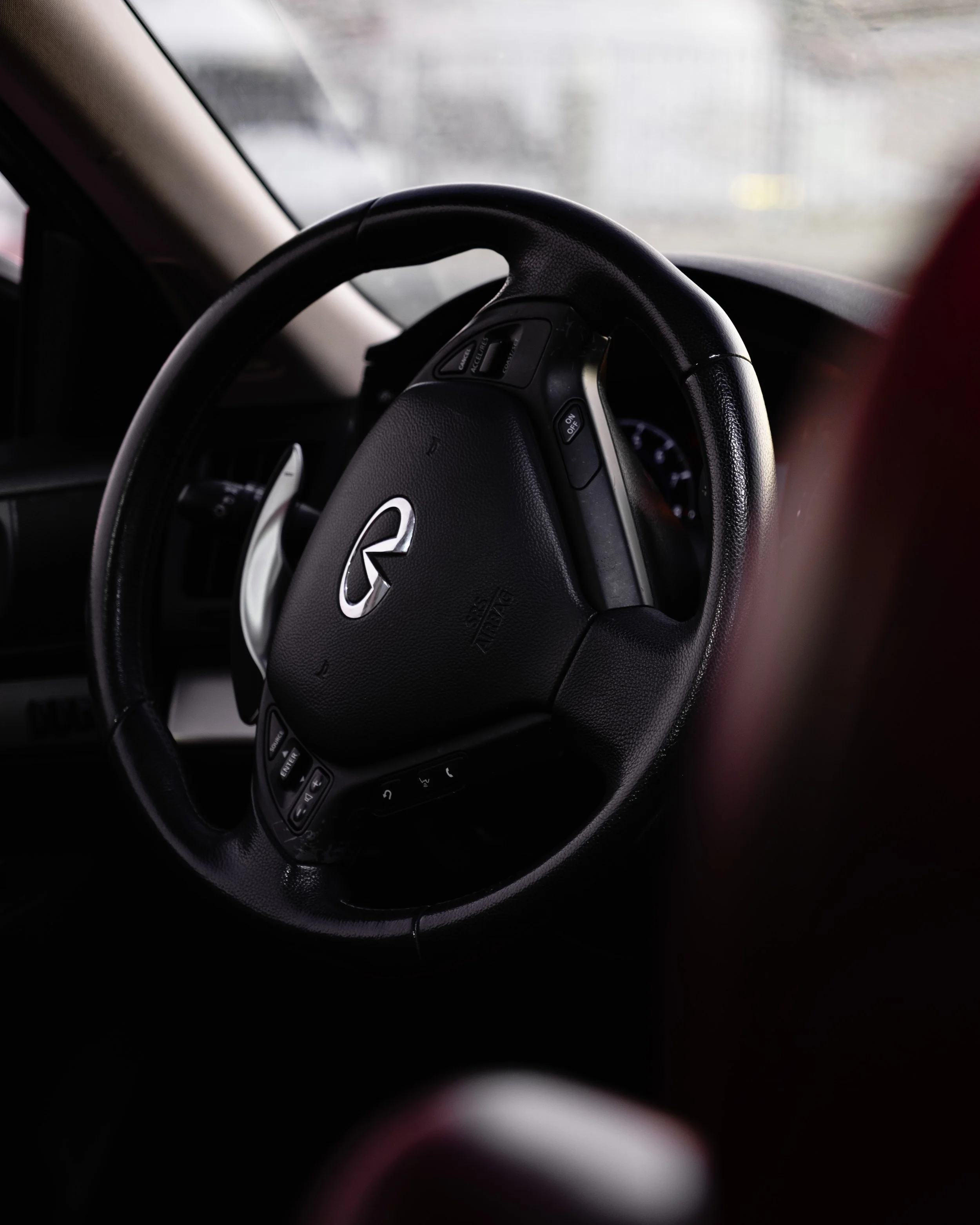 Close-up of a black Infiniti steering wheel with various control buttons, inside a car.