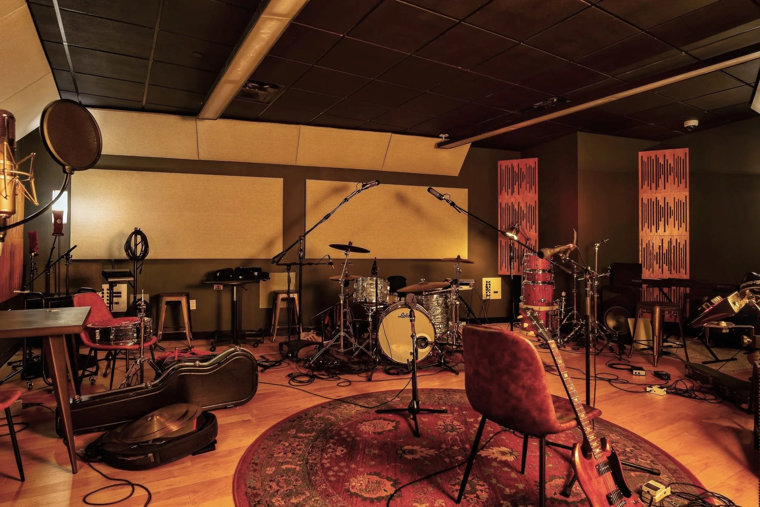Music recording studio with drum set, guitar, microphones, chairs, and soundproofing panels.