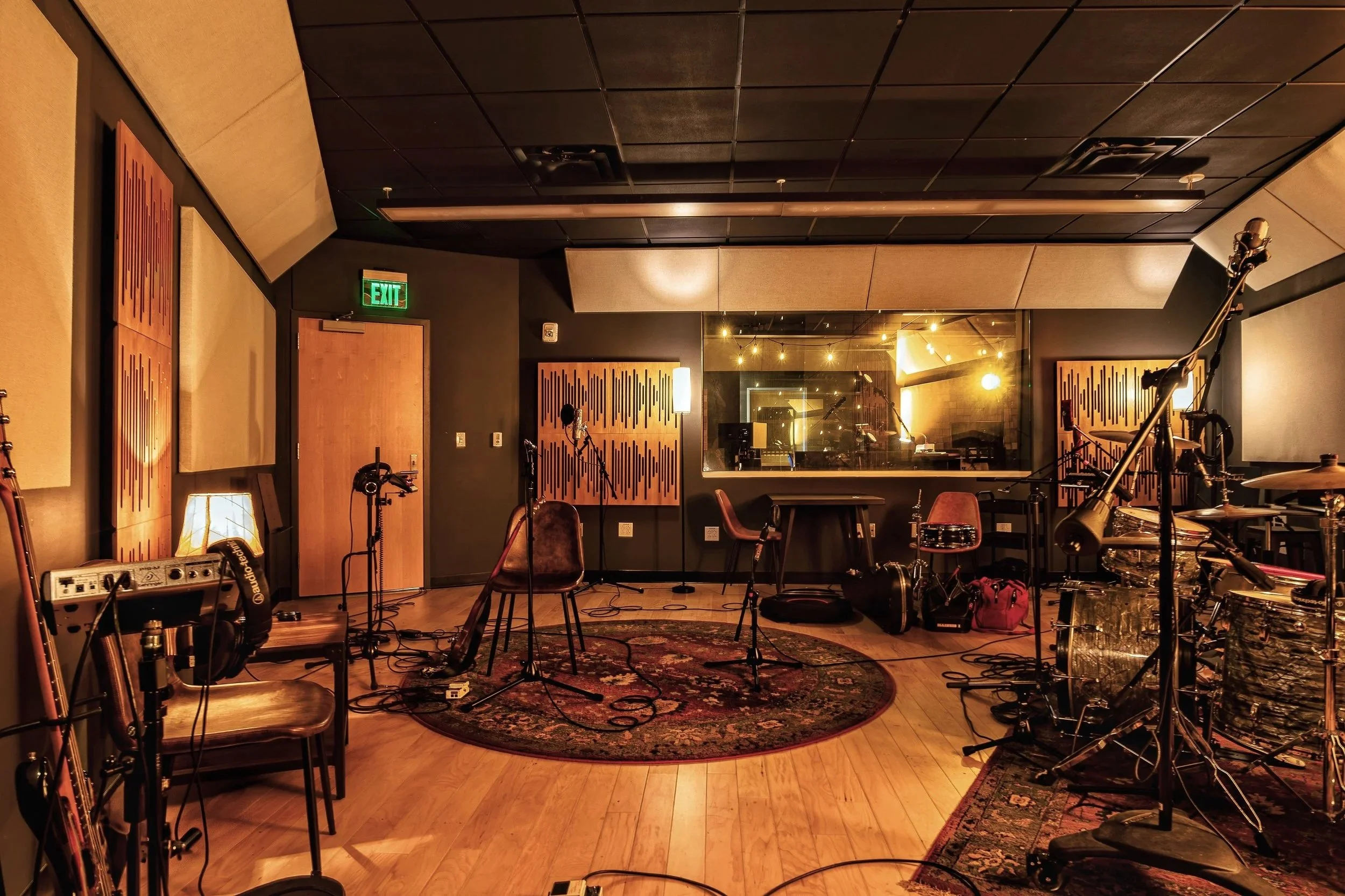 Music recording studio room with microphones, drums, guitars, chairs, and soundproofing panels.
