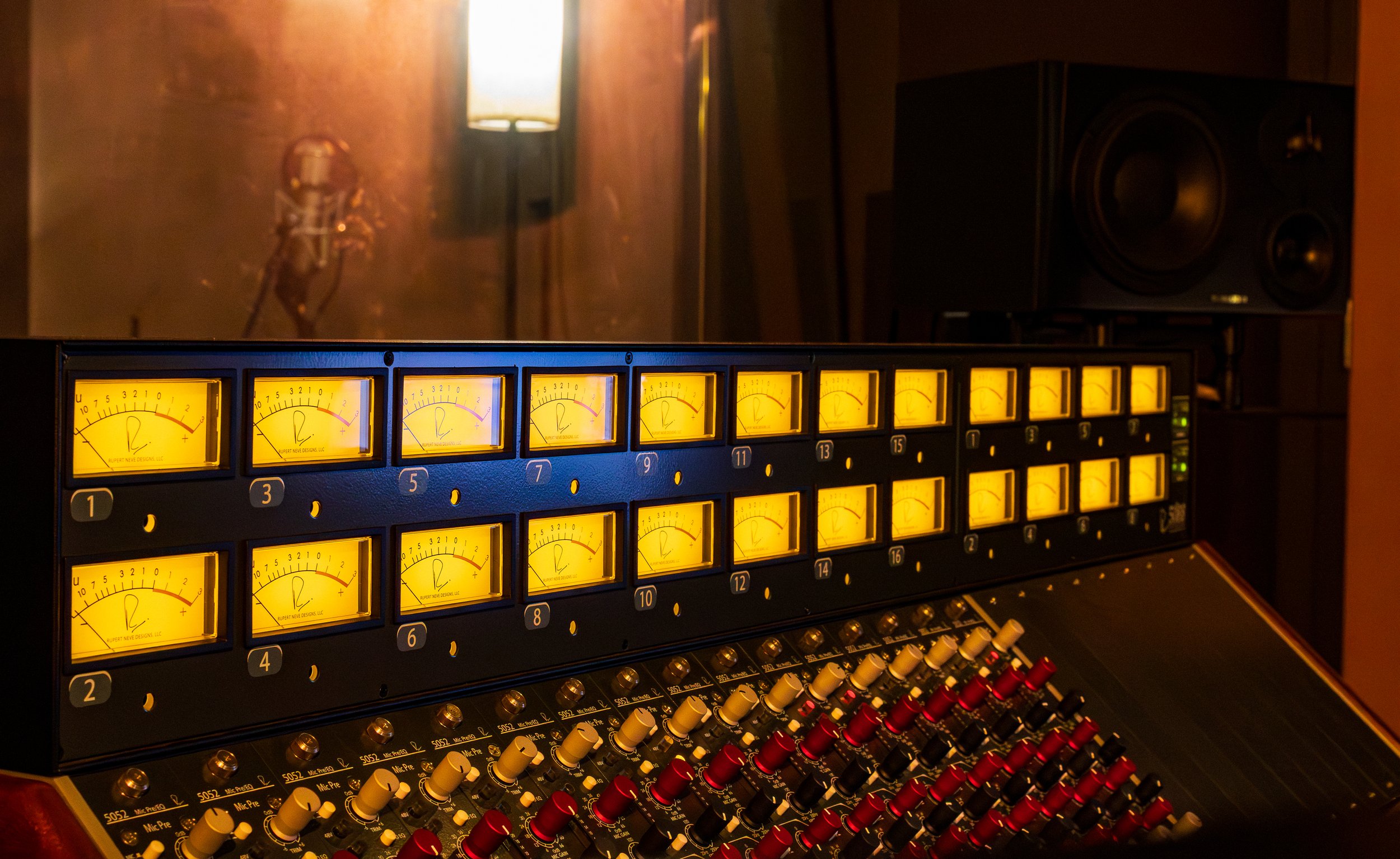 Audio mixing console with illuminated yellow VU meters and various controls in a recording studio.