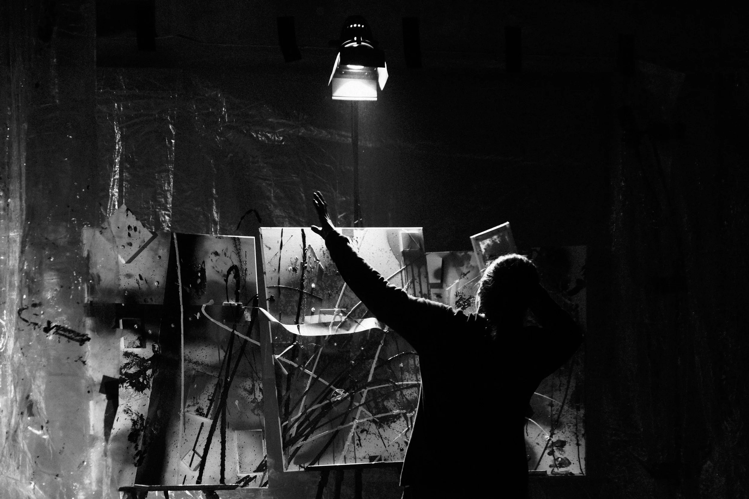 A person creating abstract painting in a dark studio, illuminated by a single overhead light