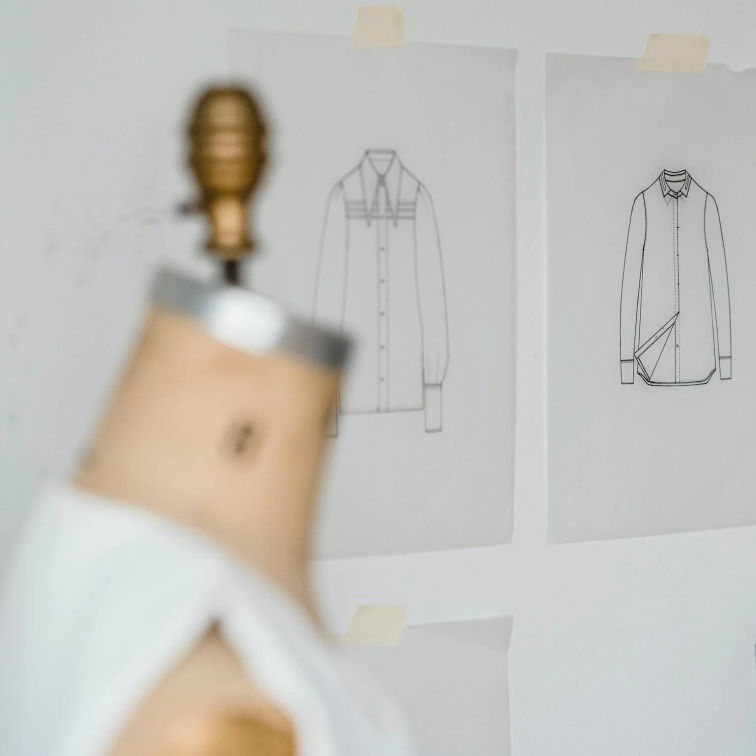 Close-up of a dress form in front of taped-up fashion sketches—representing design, patternmaking, and fashion development.