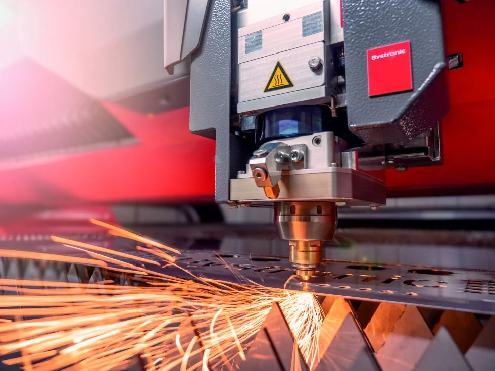 Industrial laser cutting machine operating on metal sheet, emitting sparks.