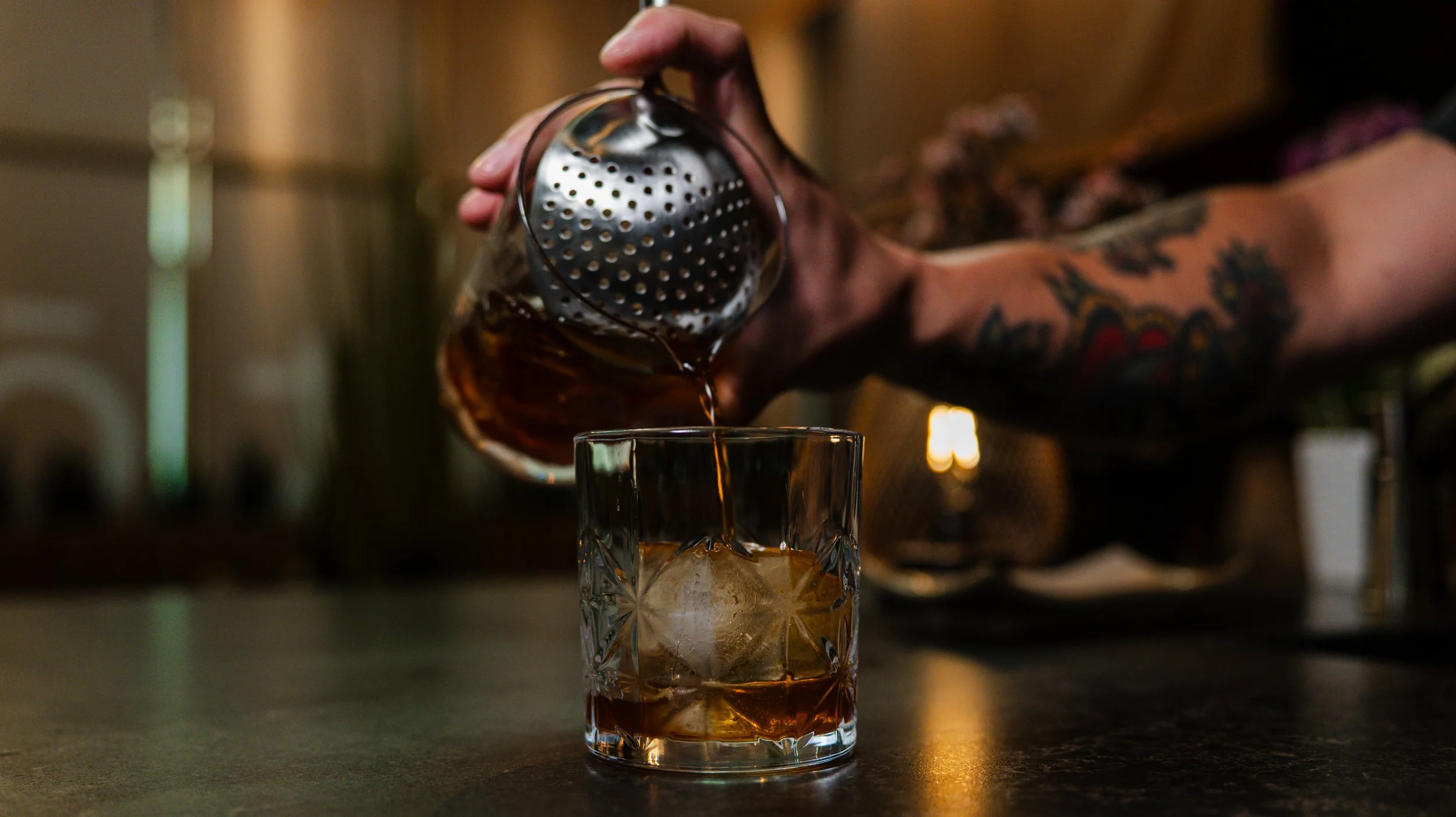 A bartender pouring a crafted Japanese whisky cocktail over a clear ice sphere at Zōtō Izakaya in Sarasota, FL.