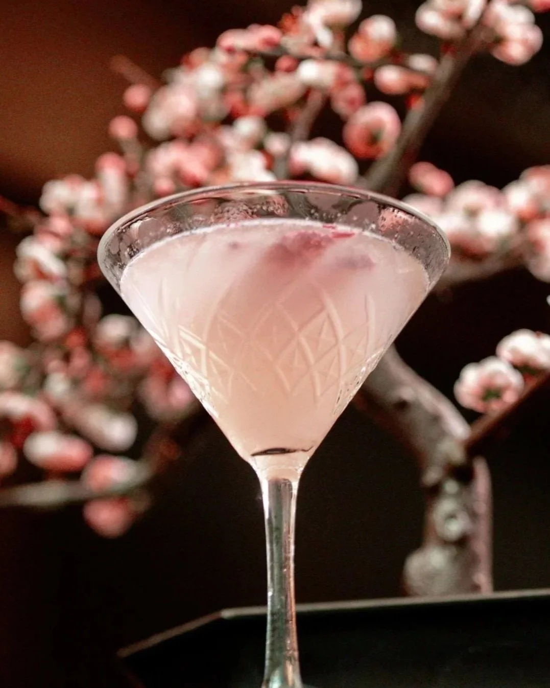 The 'Lychee-Ni-San-Chi' cocktail at Zōtō, a delicate pink lychee drink served in a crystal coupe glass with a cherry blossom background.