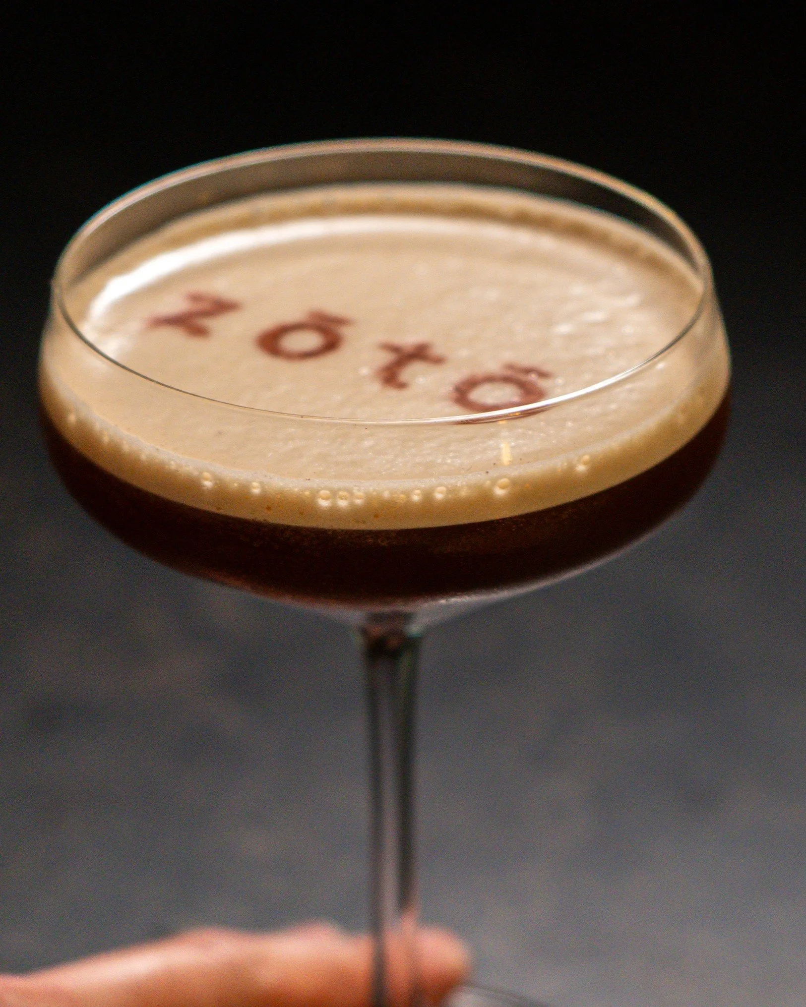 The 'The Spice is Right' cocktail featuring the Zōtō logo elegantly stenciled onto the thick foam of a dark, chilled craft cocktail.