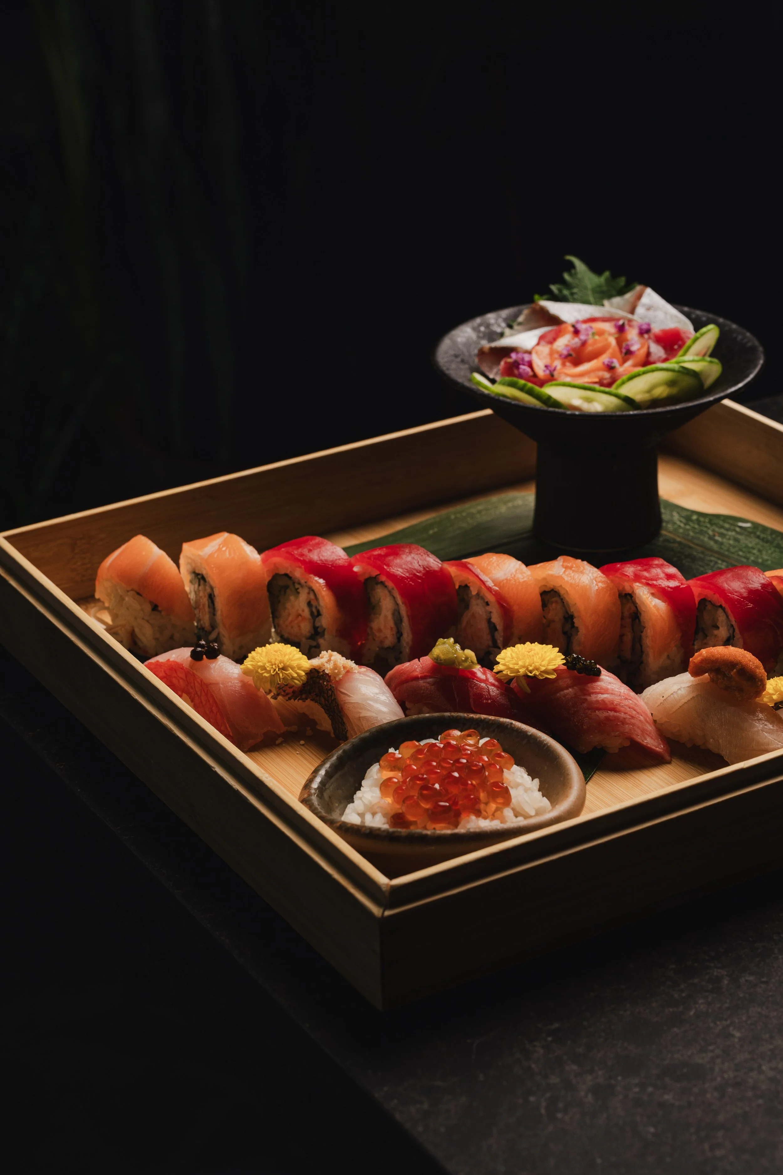 A tray of assorted sushi including nigiri and sushi rolls, with a small dish of rice topped with salmon roe, presented on a wooden serving tray.