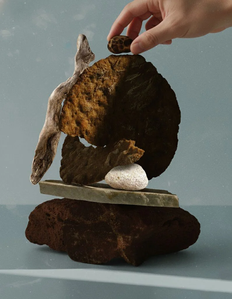 A hand placing a small pebble on top of a stack of rocks and stones of various sizes and textures, balanced on a flat surface.