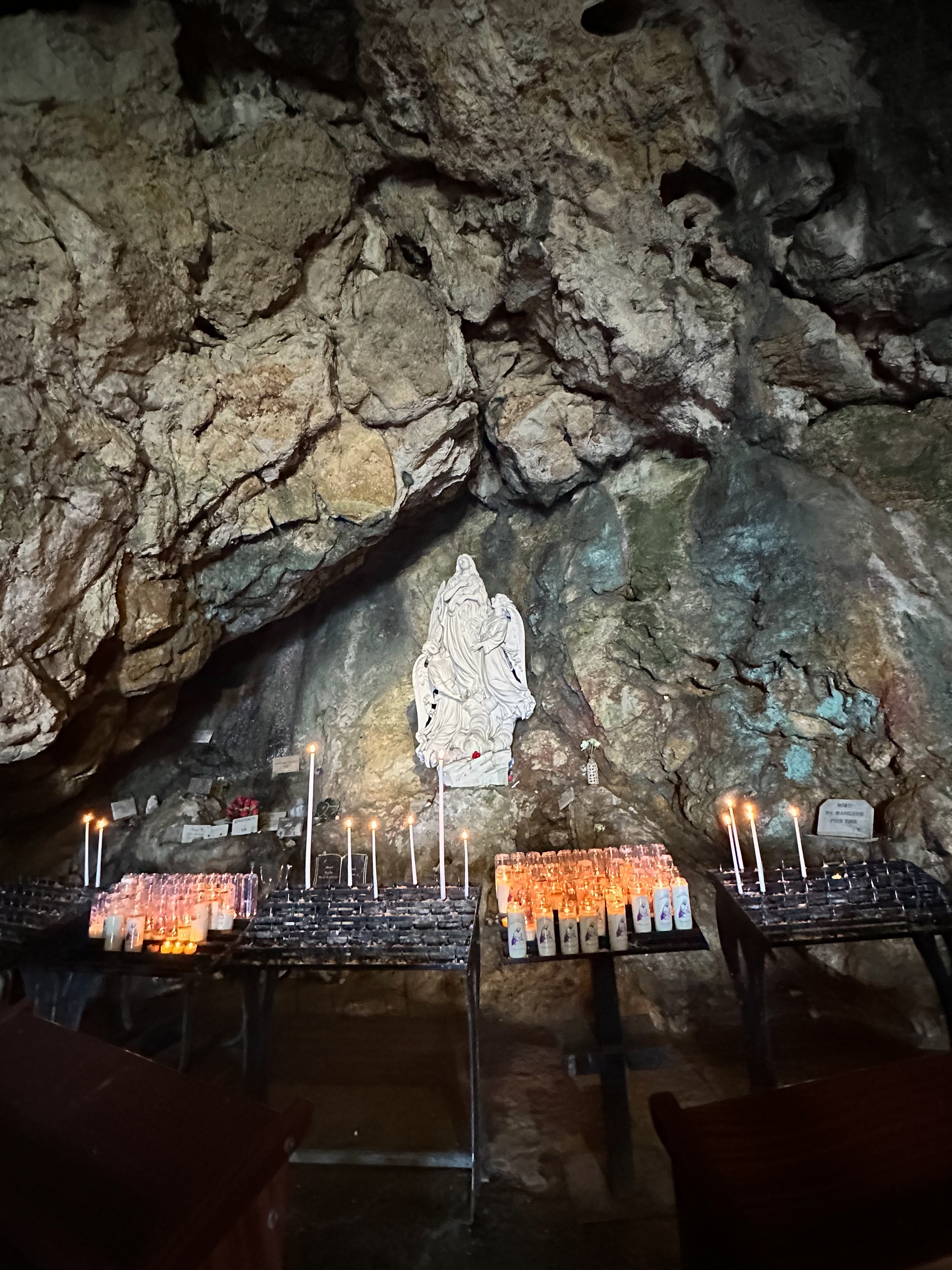 A shrine with candles and images of religious figures inside a rock cave.