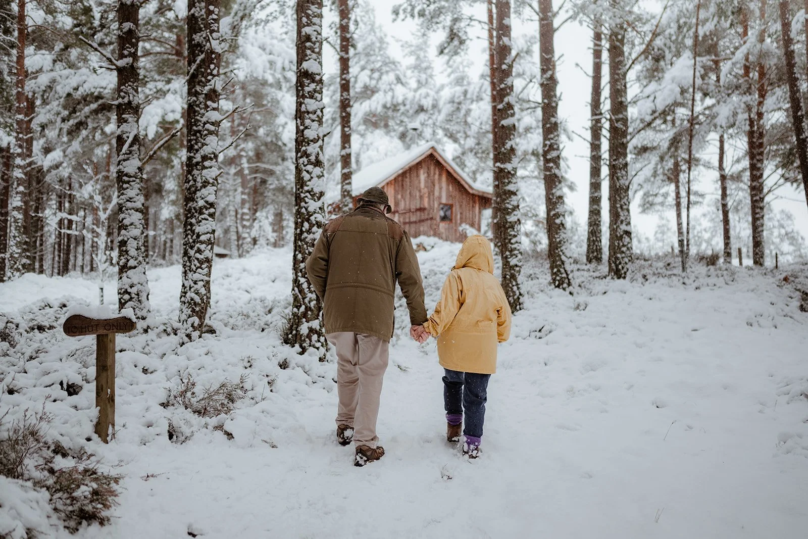 a couple walking up to an off-grid cabin through a snow covered forest
