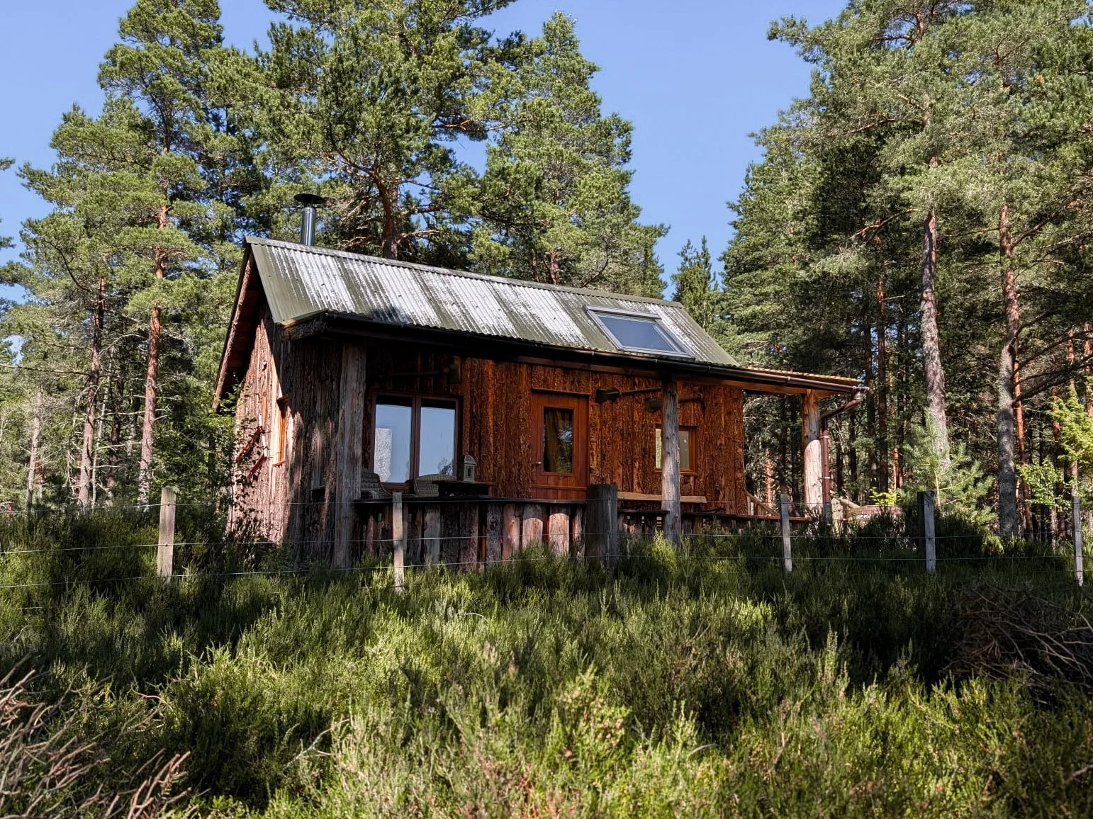 An off-grid hut in the cairngorms national park surrounded by scots pine forest with a wood-burning stove, whisky barrel in front and outdoor bucket shower to one side