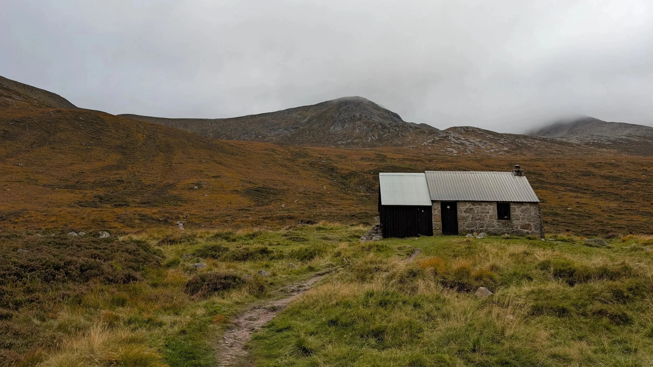A scottish bothy in the mountains with grass around and hills in the background