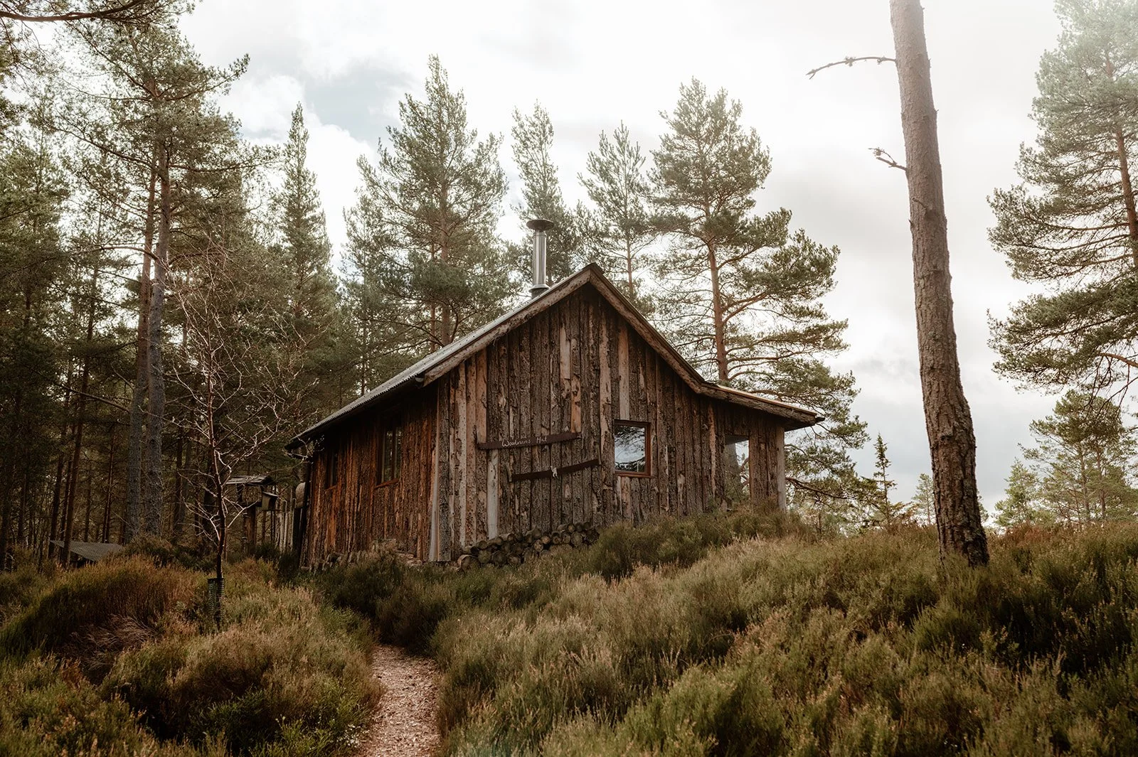 A wooden off-grid hut situated on the edge of a forest with views across towards the mountains