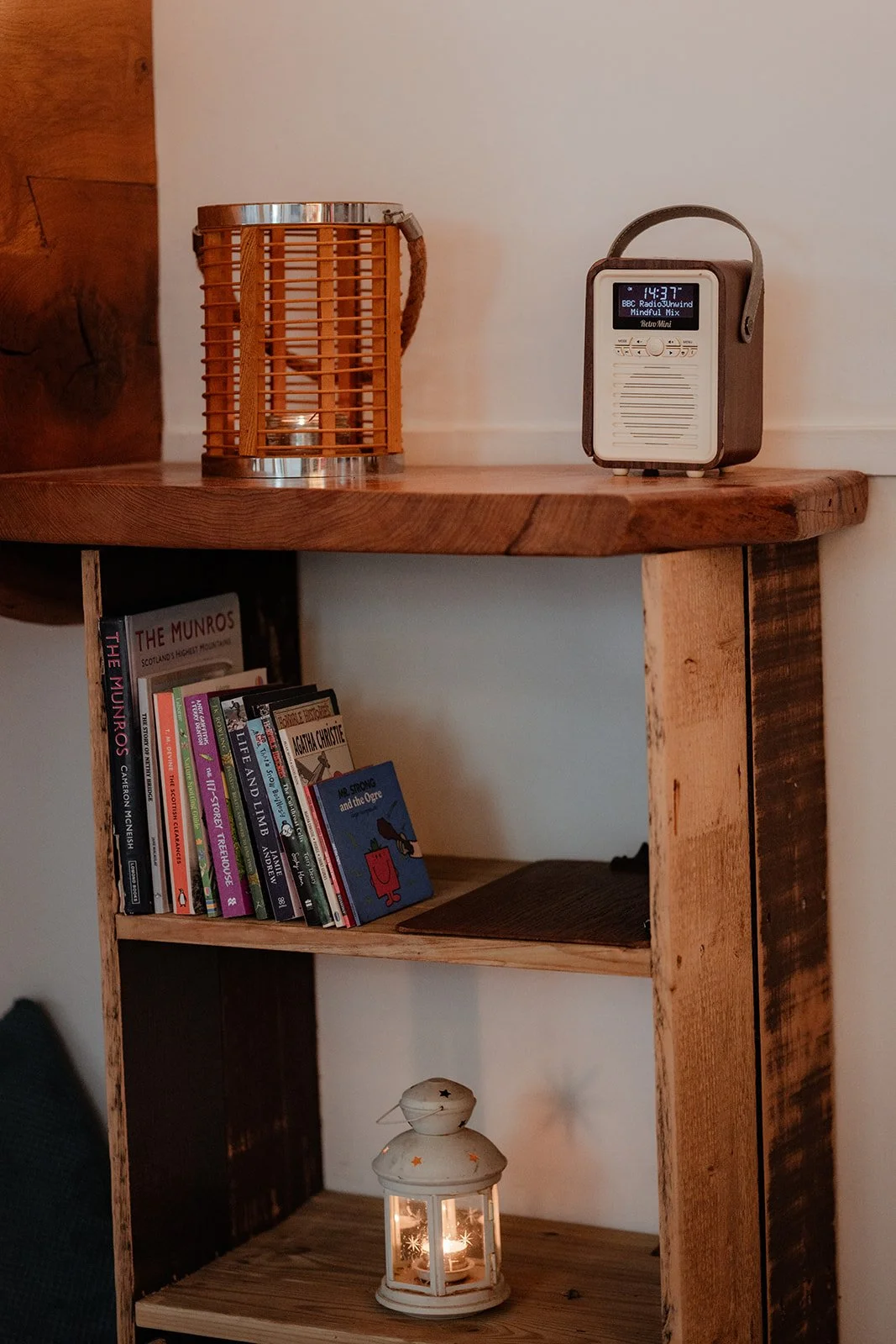 A wooden shelf with books, a decorative lantern, and a portable radio on top.