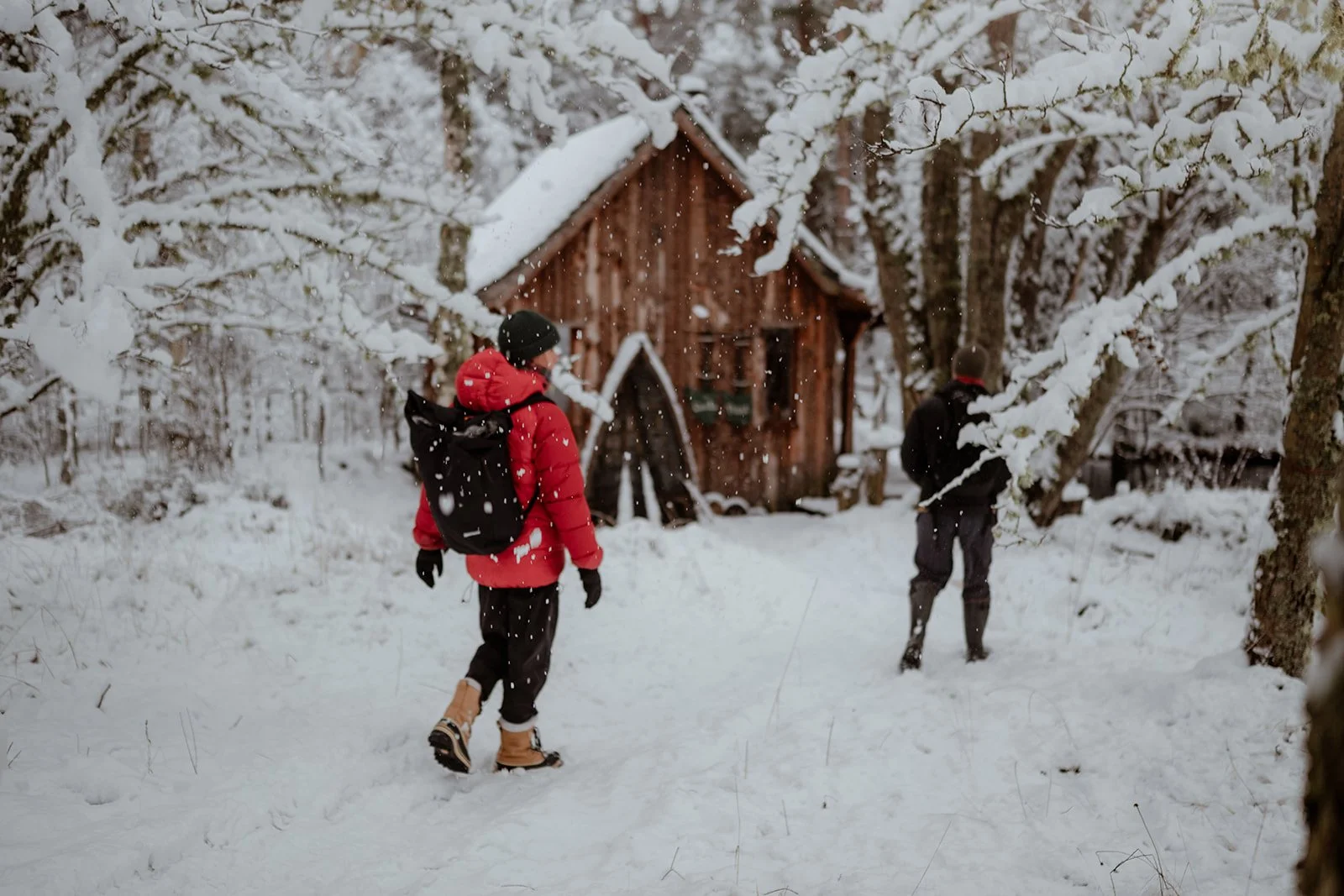 A couple walking through a snow covered forest towards an off-grid forest hut in the Cairngorms National Park