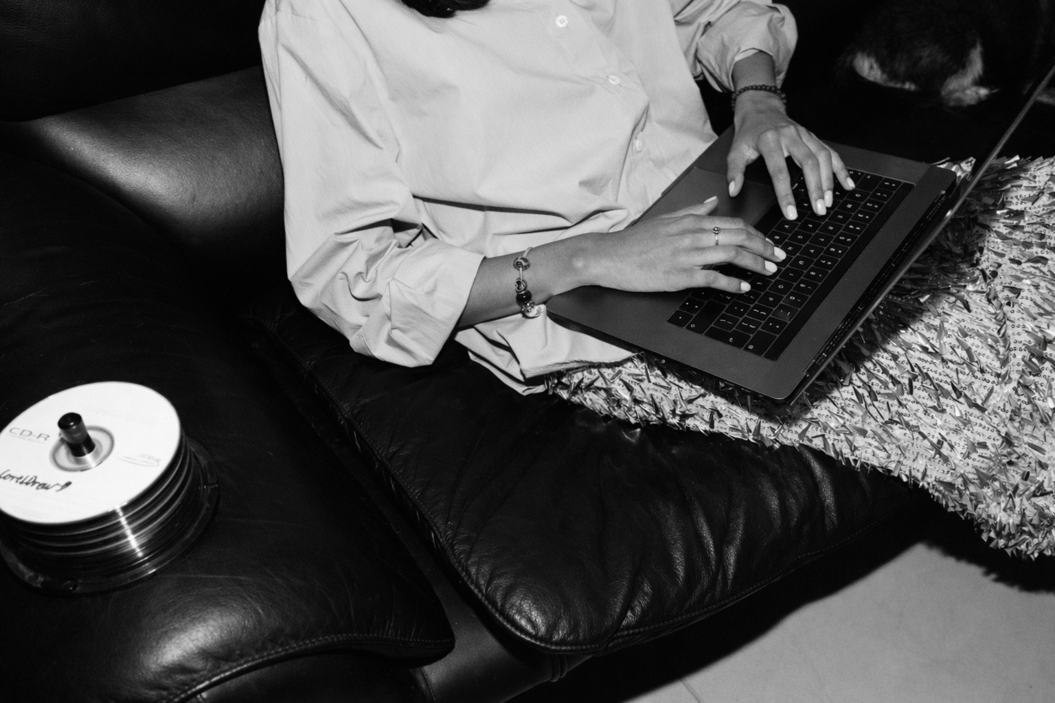 Person lying on a couch using a laptop, with a stack of CDs nearby.