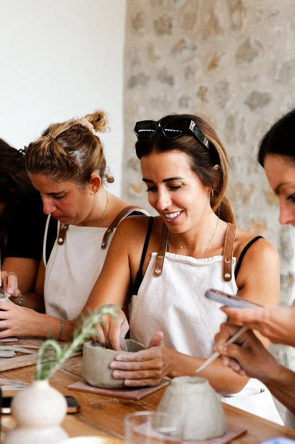 Un grupo de mujeres participando en una clase de cerámica, trabajando con arcilla sobre una mesa de madera