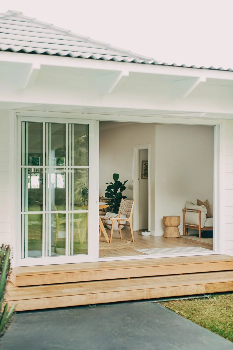 Sliding glass doors slide fully open to merge a warm timber deck with a light-filled living space styled with natural materials and indoor greenery, the seamless connection found in healthy homes in Dee Why