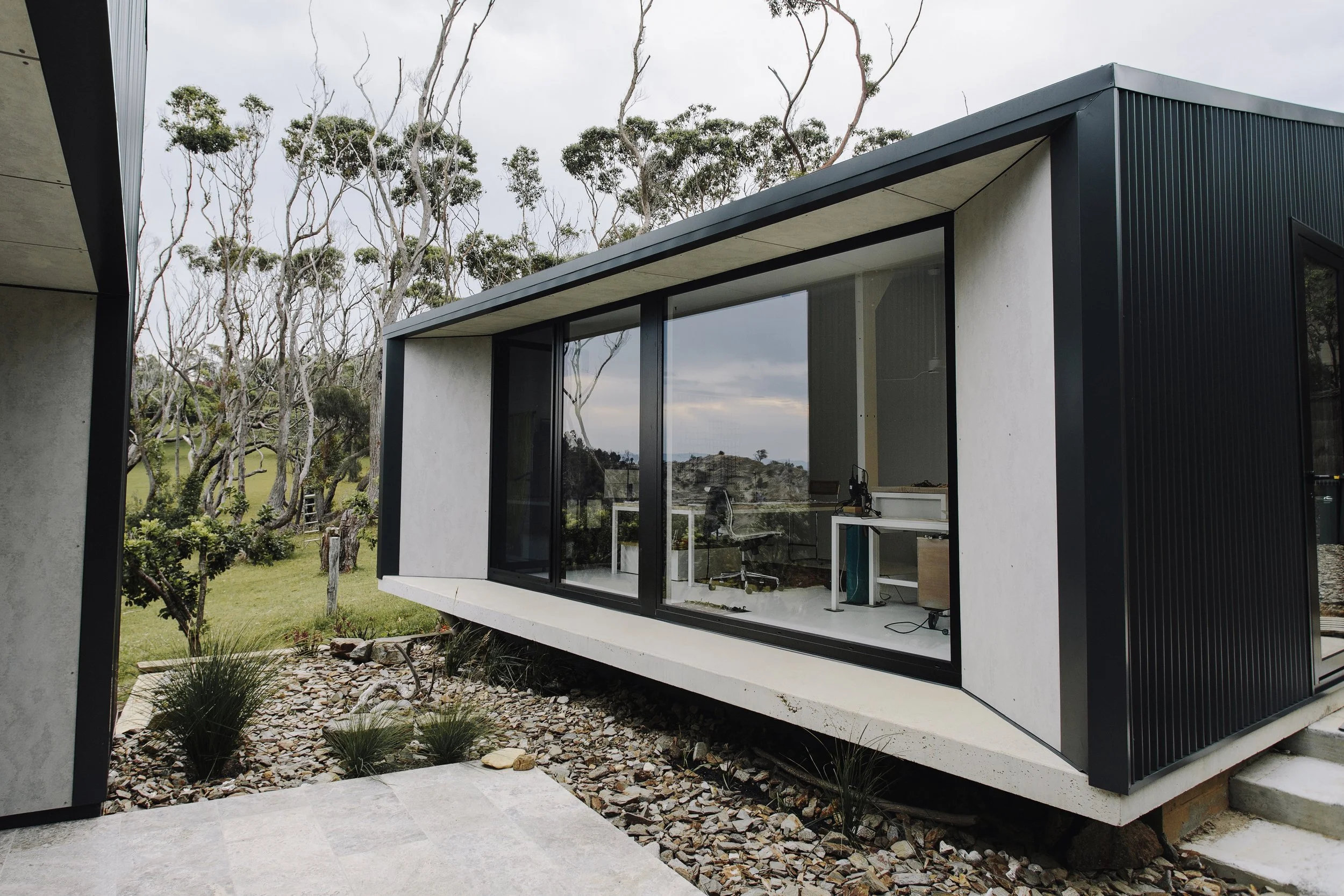 Modern architectural design featuring expansive glass windows and natural stone landscaping, showcasing the quality craftsmanship found in granny flats in North Shore and luxury home extensions