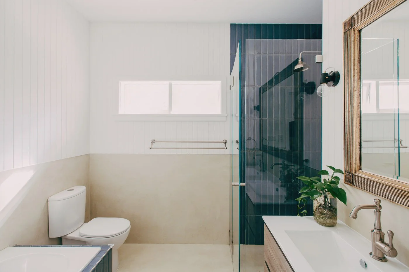 Modern bathroom with glass shower, dark tiles and wooden-framed mirror at a custom extension renovation in Kenthurst