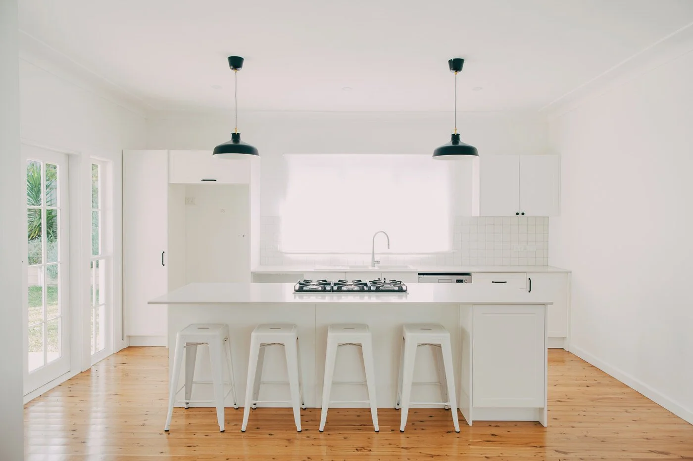 Bright white kitchen with island, black pendant lights and gas cooktop in a Beecroft custom extension featuring timber flooring