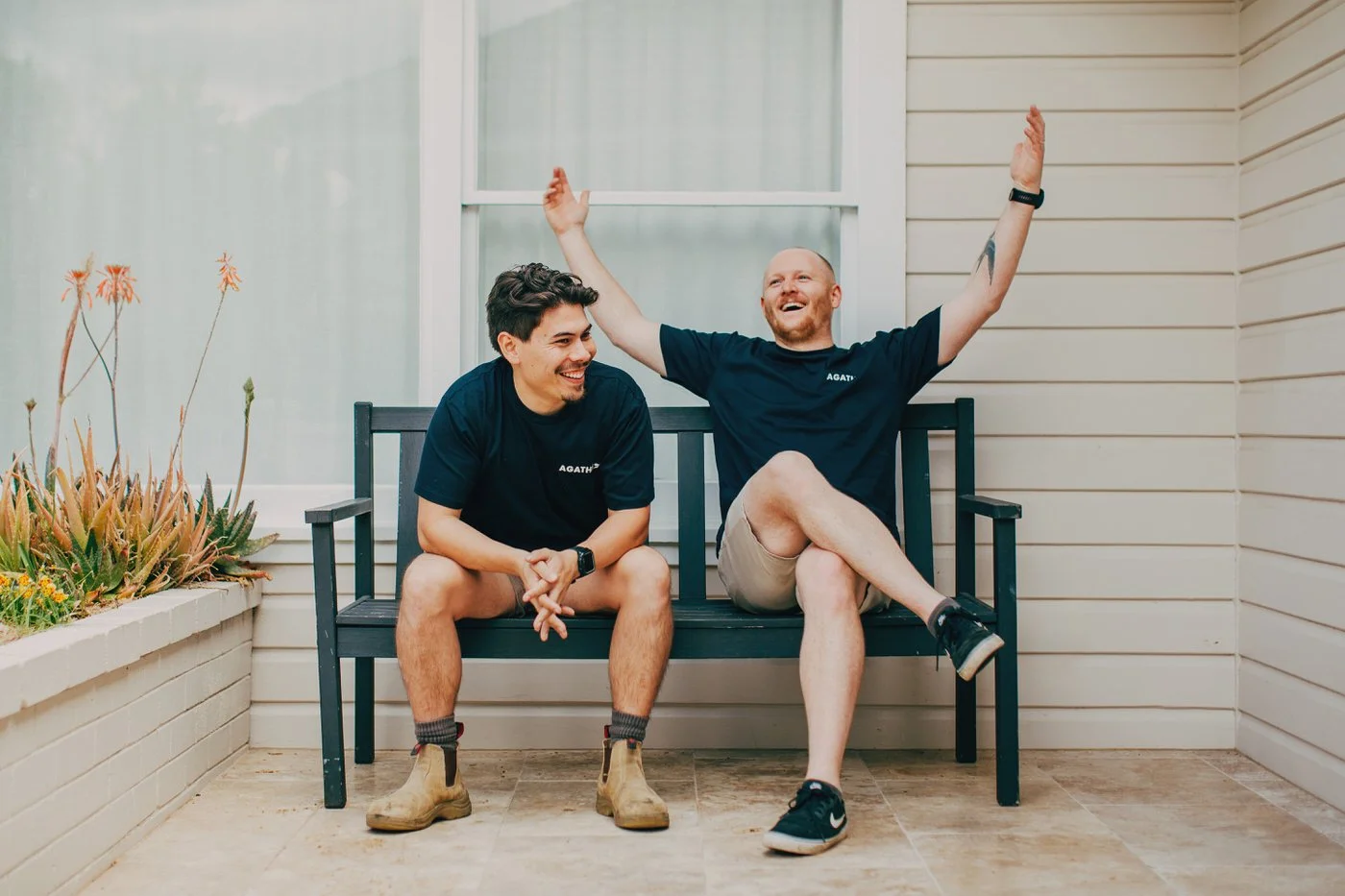 Two Agathē team members relaxing and laughing on a bench outside a renovated home, proud of creating Healthy Homes in Northern Beaches.