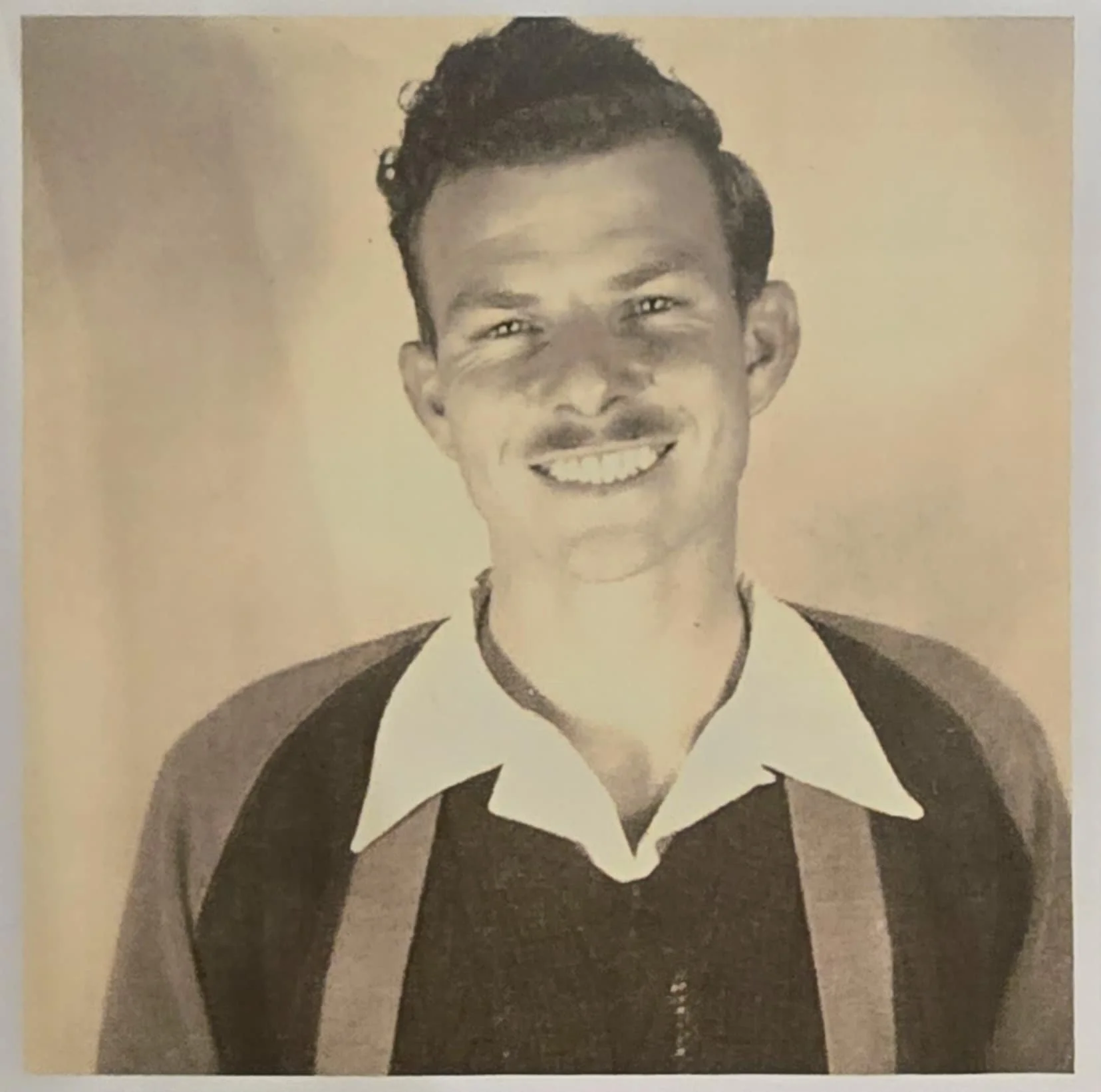 Black and white vintage photo of a smiling man wearing a collared shirt and sweater with stripes.