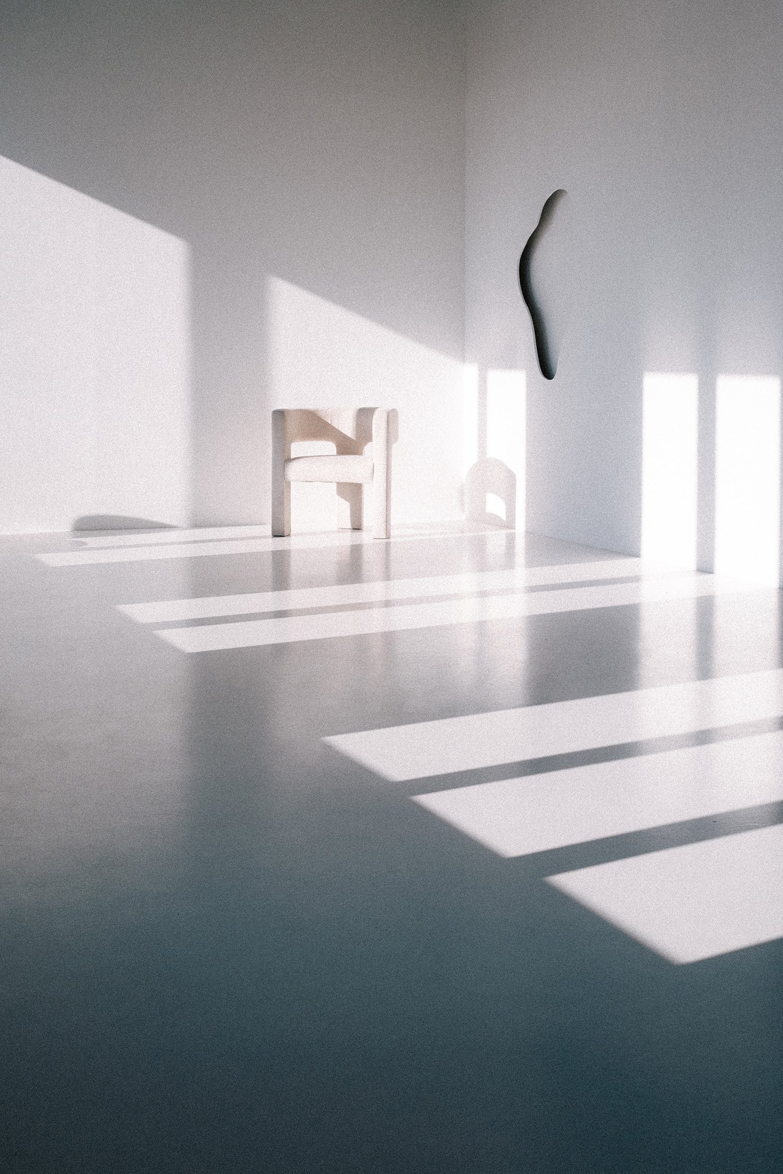 Minimalistic room with a small white chair, abstract wall sculpture, and shadows cast by window blinds.