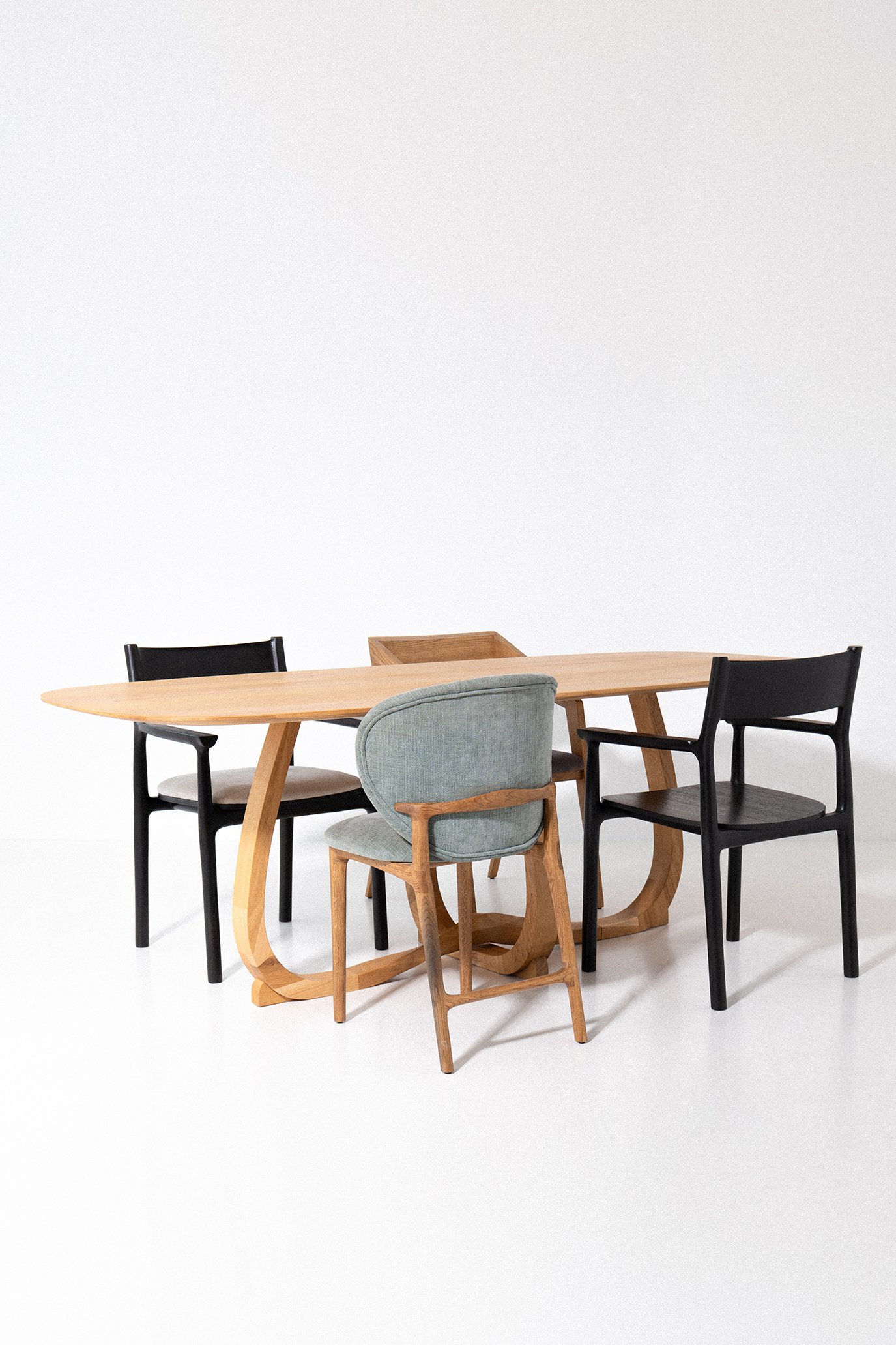 A wooden dining table with four chairs, one upholstered in light blue fabric, and the others in black with wooden legs, set against a plain white background.
