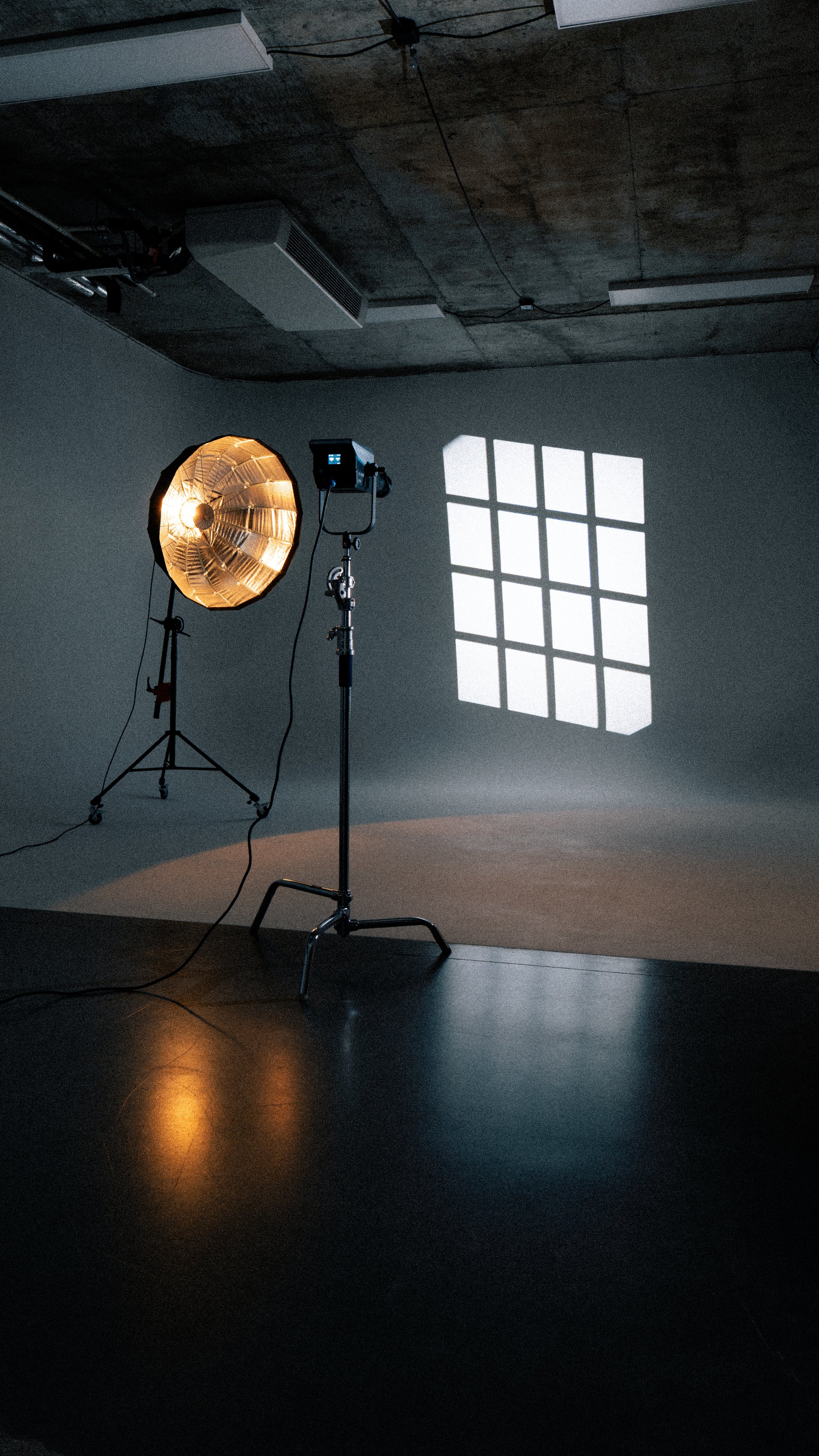 Photography studio with a large studio light and a spotlight, casting a shadow of a window with 12 panes onto the wall.