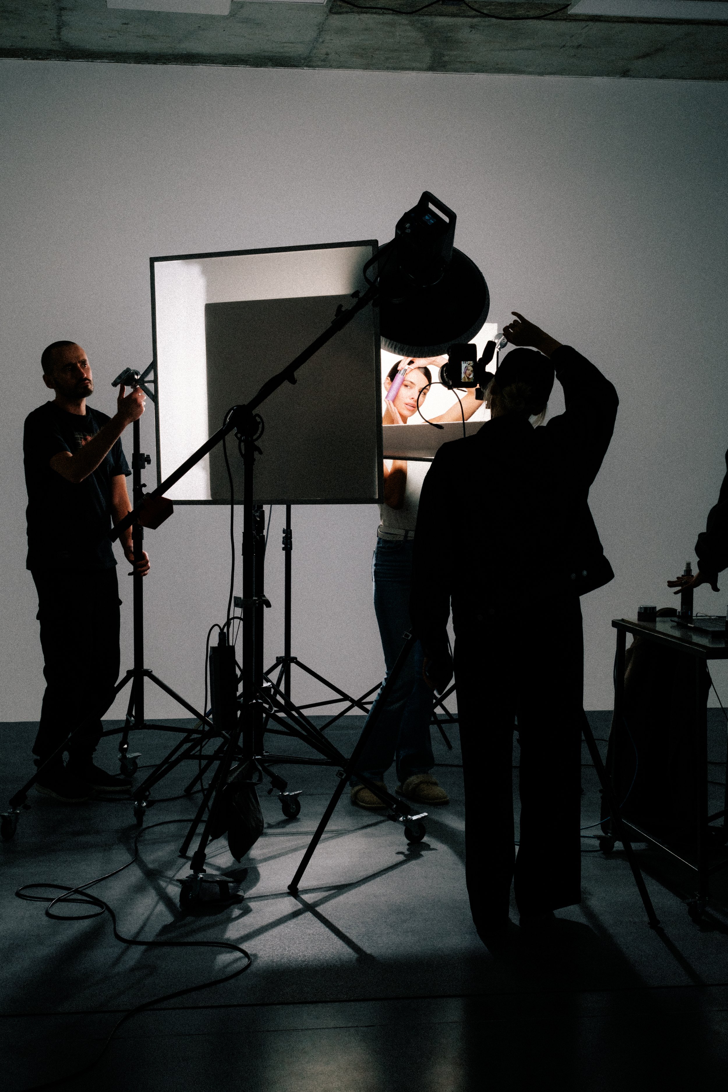A photoshoot setup with a model, photographers, and lighting equipment in a studio