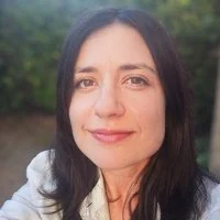 Close-up of a woman with dark hair smiling outdoors