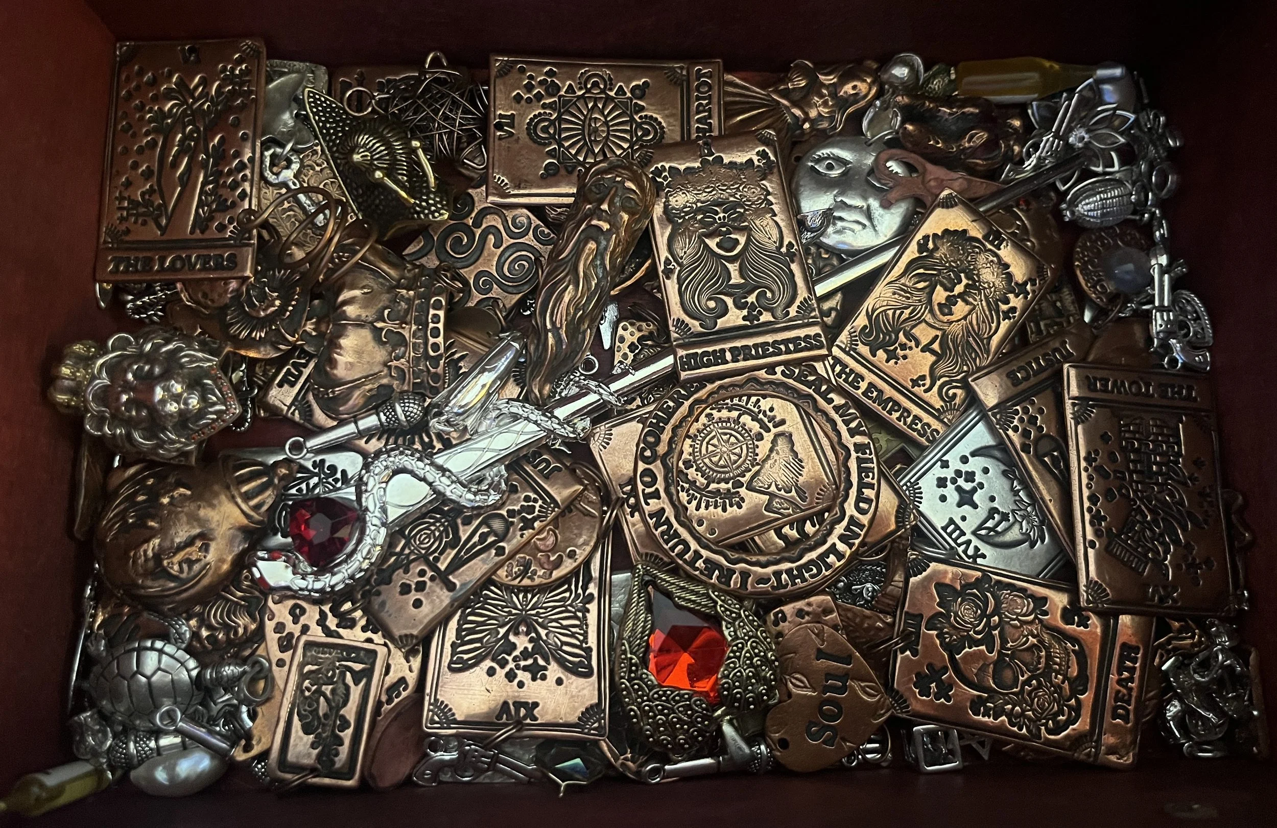 A collection of various metal charms and pendants, including animals, faces, symbols, and characters, in a box.
