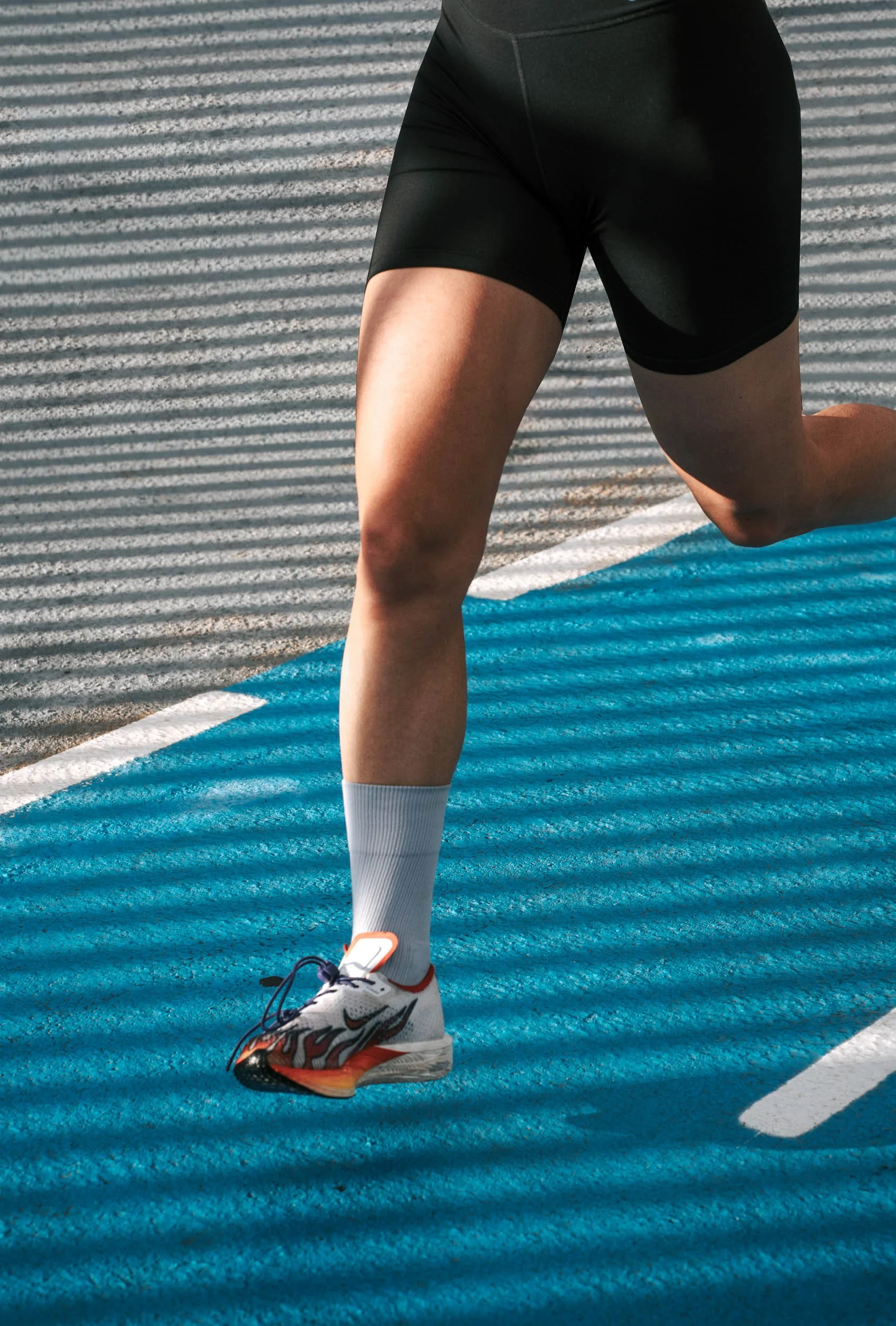 A person in athletic wear is in a forward lunge position on a blue running track, with striped shadows from sunlight.