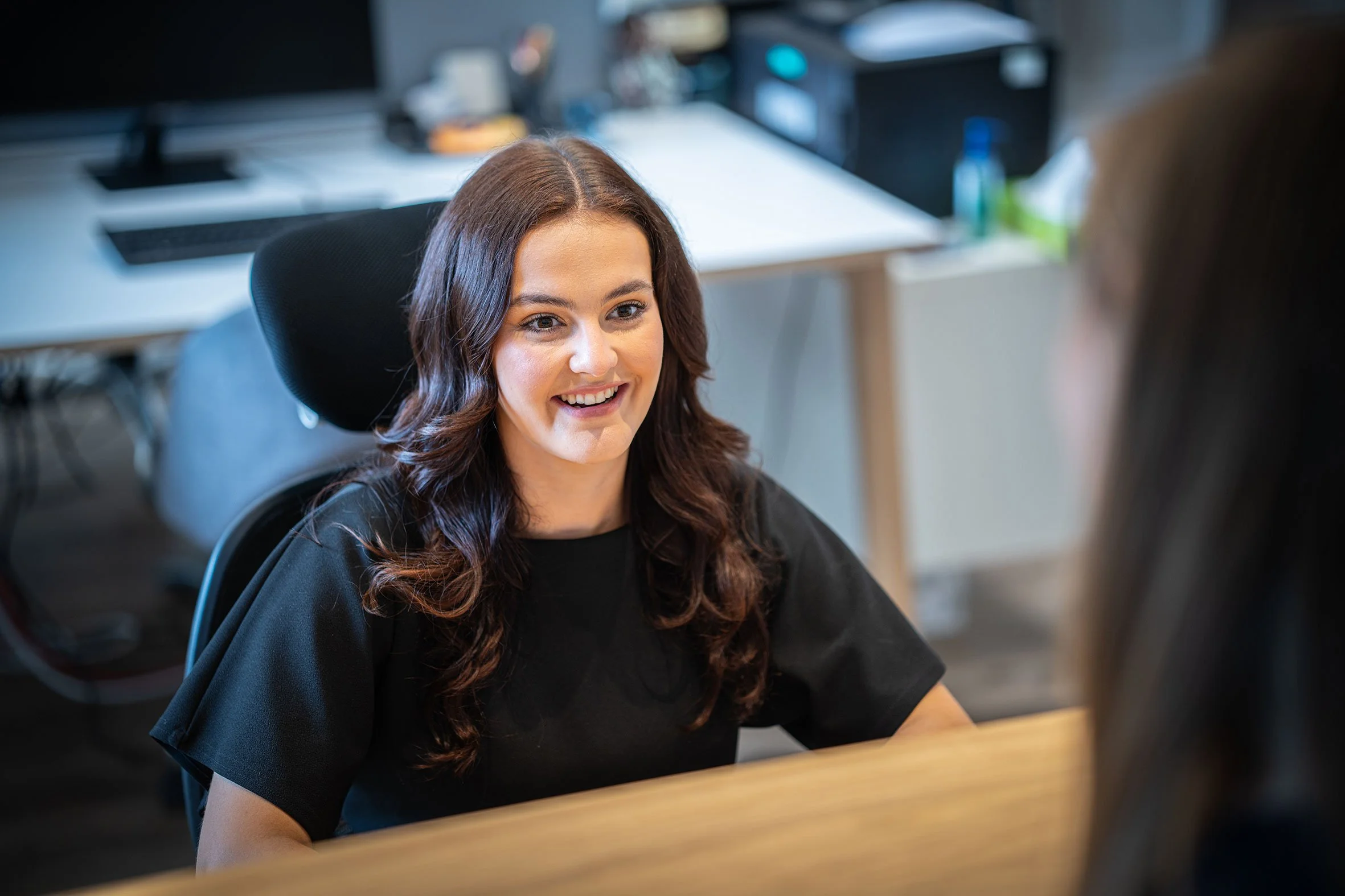 Sophie Bell smiling and talking to another person in an office setting.